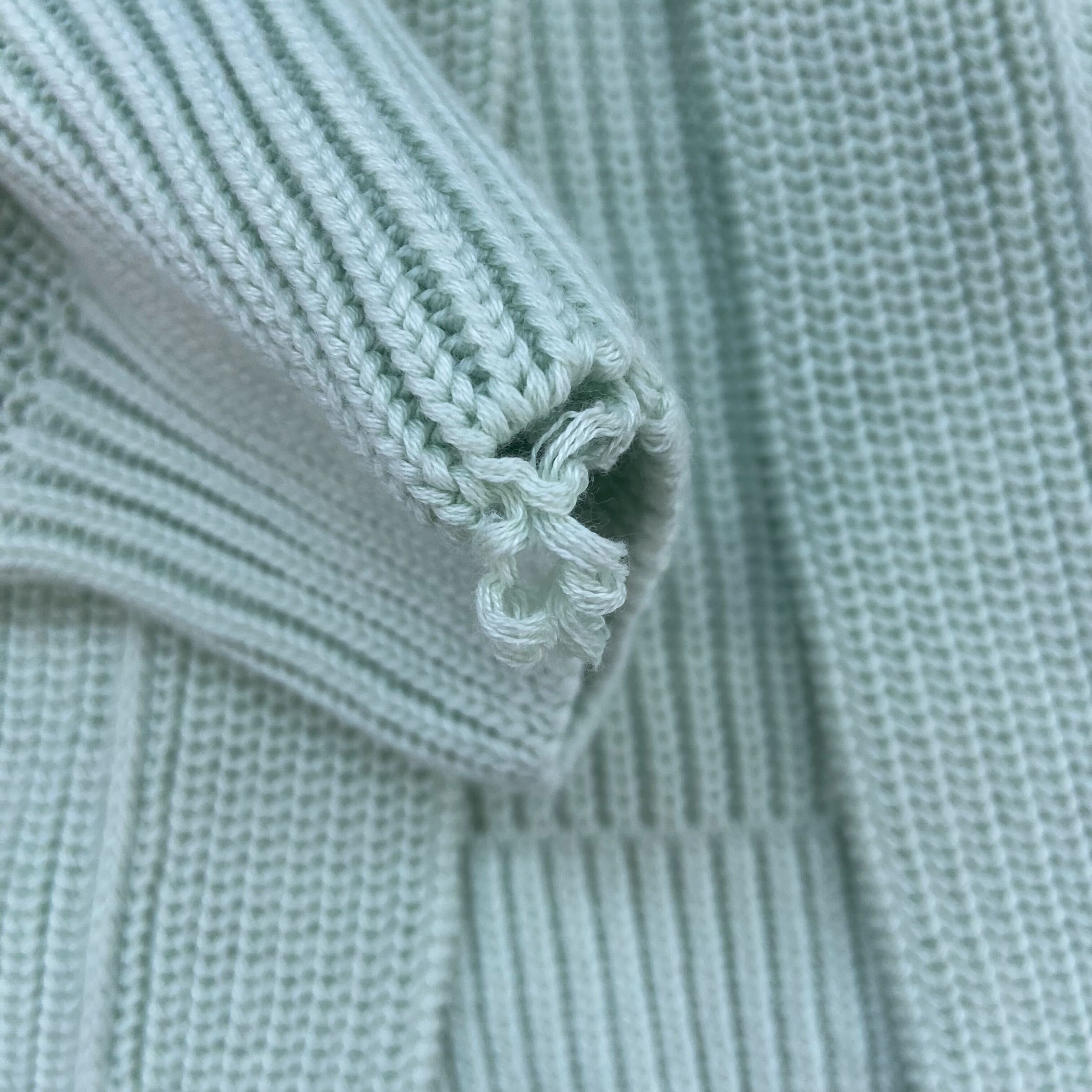 Hellgraues Strickgewebe mit feinem Rippmuster und lockerem Fadenende.