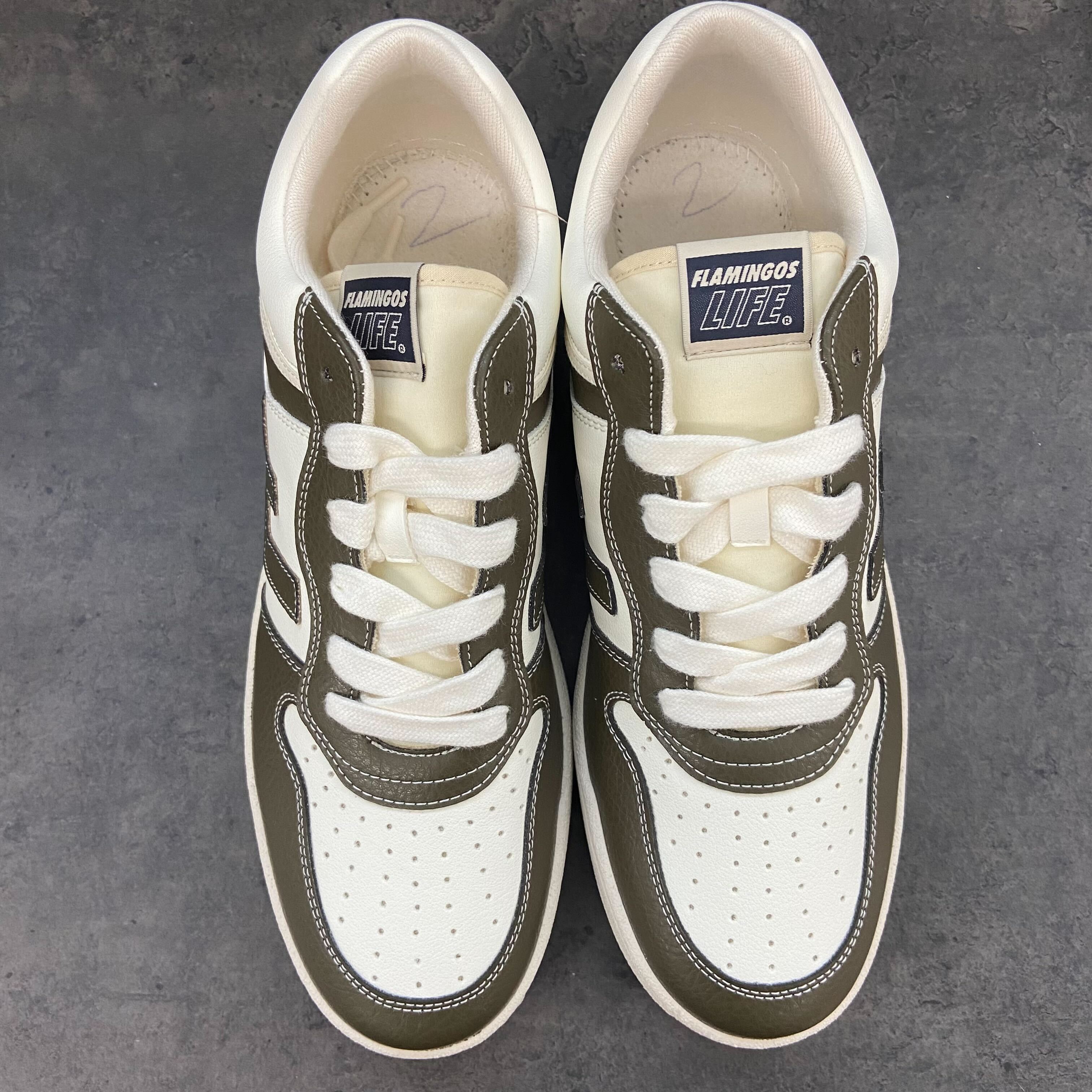 Ein Paar weiße und olivgrüne Sneaker mit der Aufschrift "Flamingos Life" auf dem Etikett, auf grauem Hintergrund.
