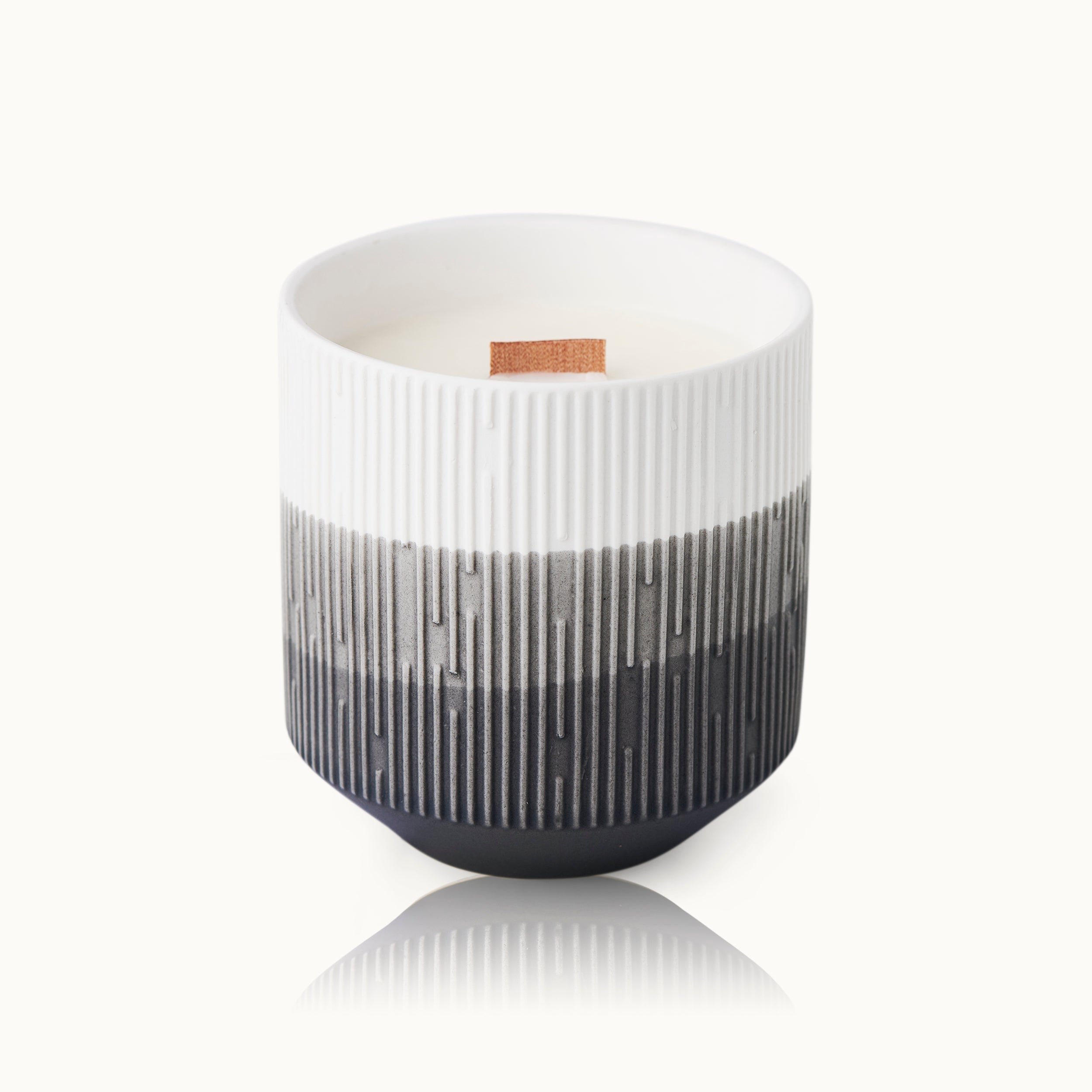 Kerze in einem gestreiften Becher mit Holzdocht, schwarz-weißes geometrisches Muster, auf weißem Hintergrund.