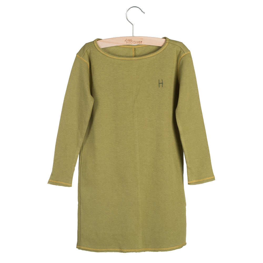 Ein einfaches, langärmeliges, olivgrünes Kleid für Kinder hängt an einem Holzbügel. Das Kleid hat einen kleinen Buchstaben H auf der linken Brust und ist an den Säumen gesäumt.
