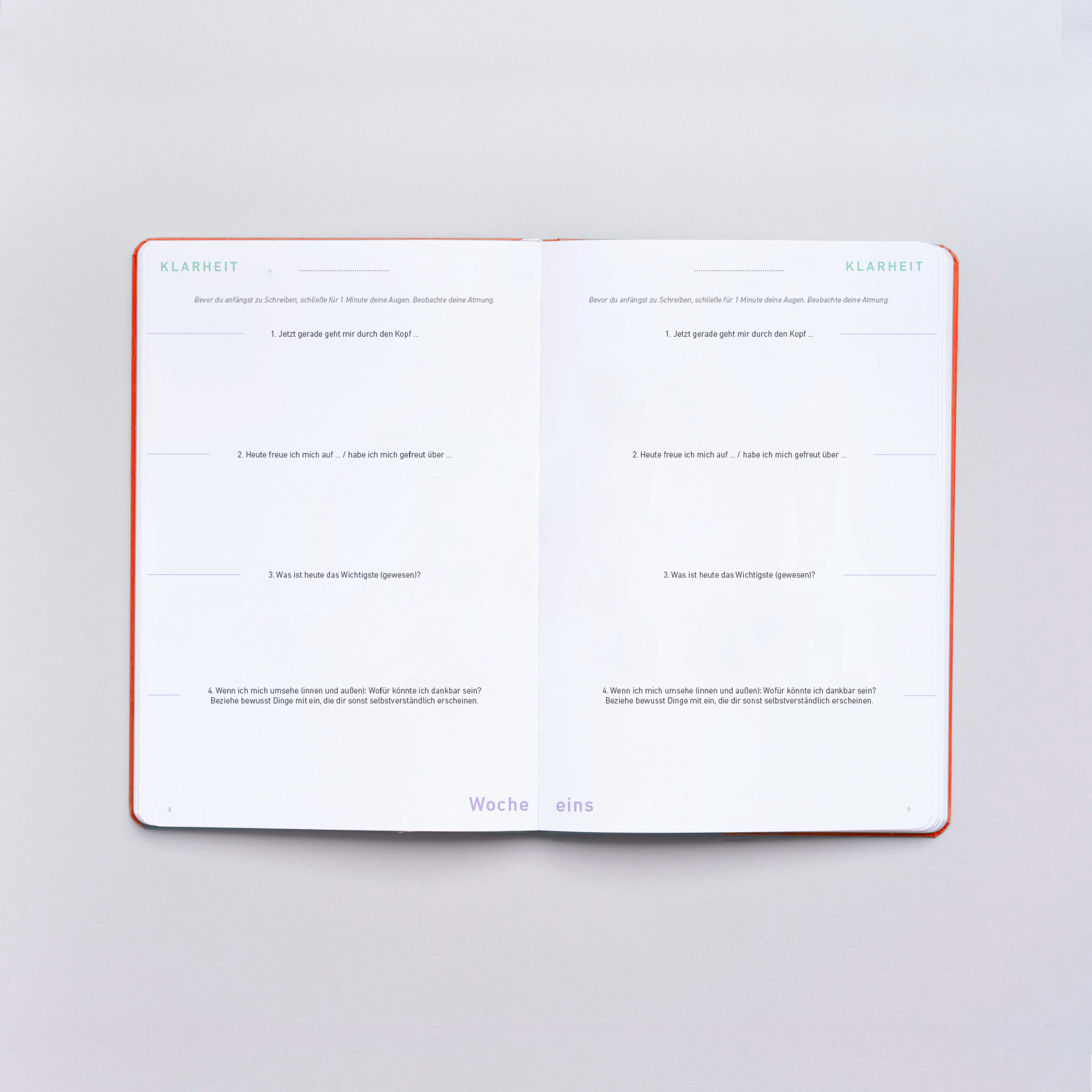 Aufgeschlagenes Notizbuch mit Fragen zur Reflexion auf beiden Seiten, markiert mit "Klarheit" und "Woche eins".