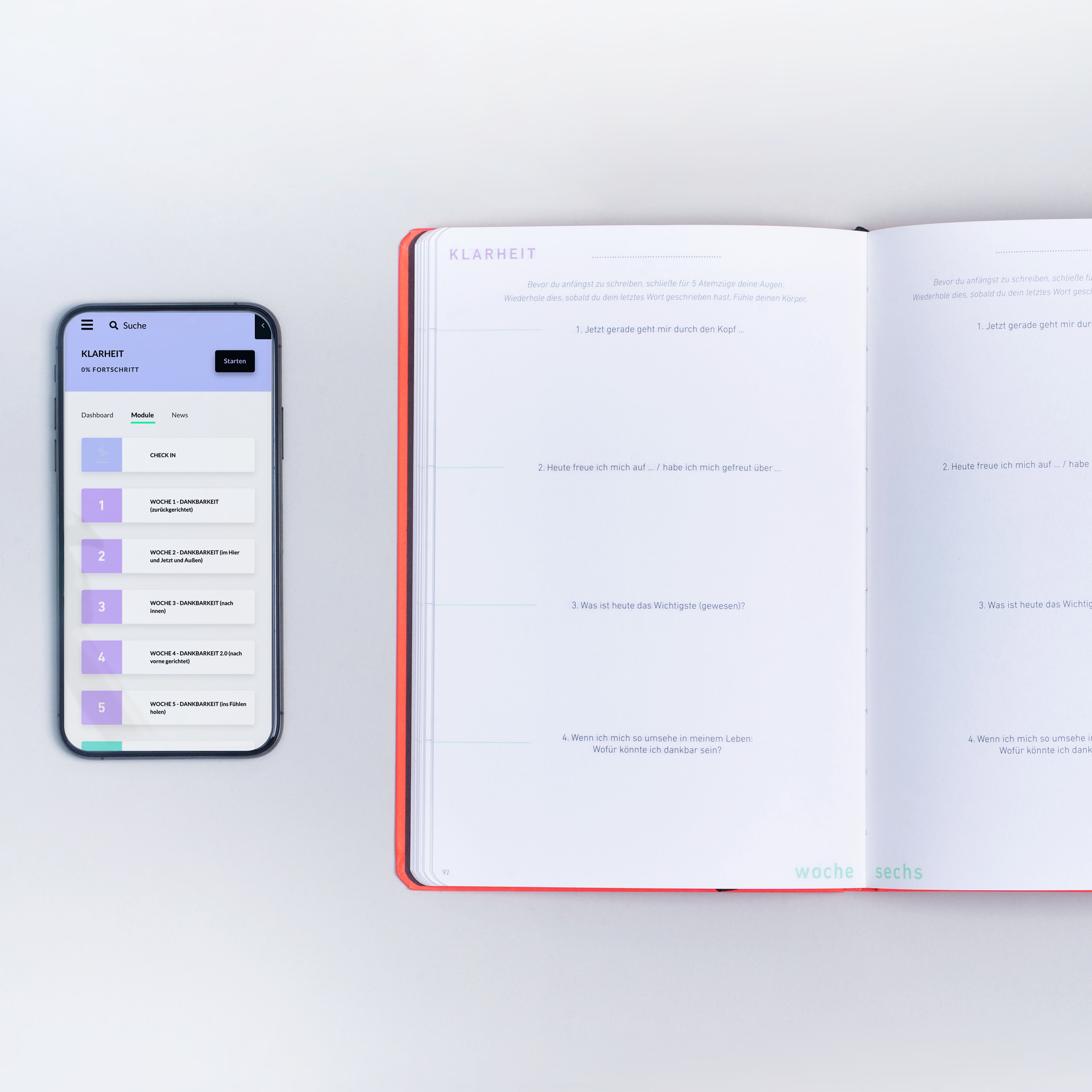 Smartphone mit geöffneter App neben einem aufgeschlagenen Planer mit Fragen und rotem Rand auf einem Tisch.