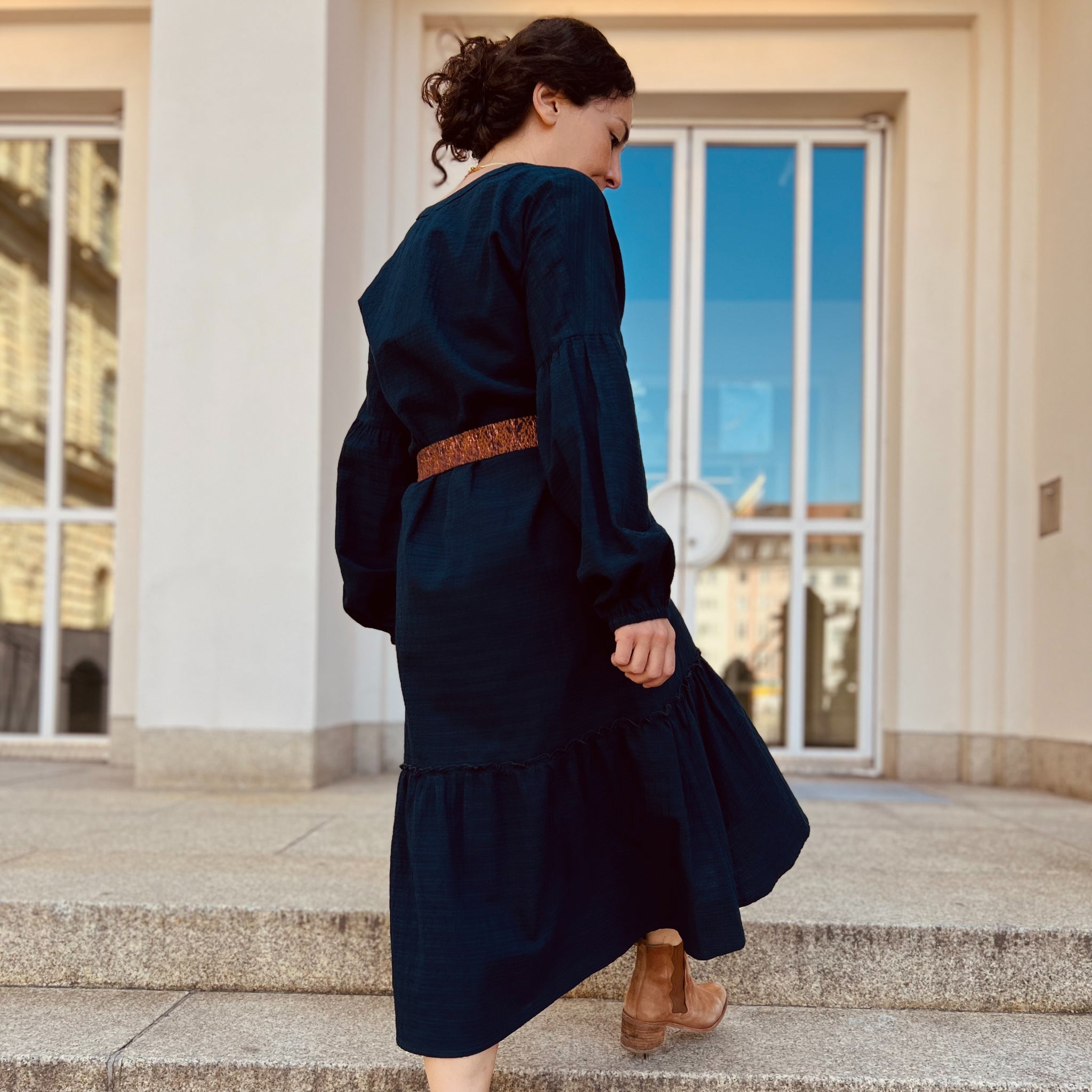 Eine Person in einem langen dunkelblauen Kleid steigt eine Steintreppe hinauf.
