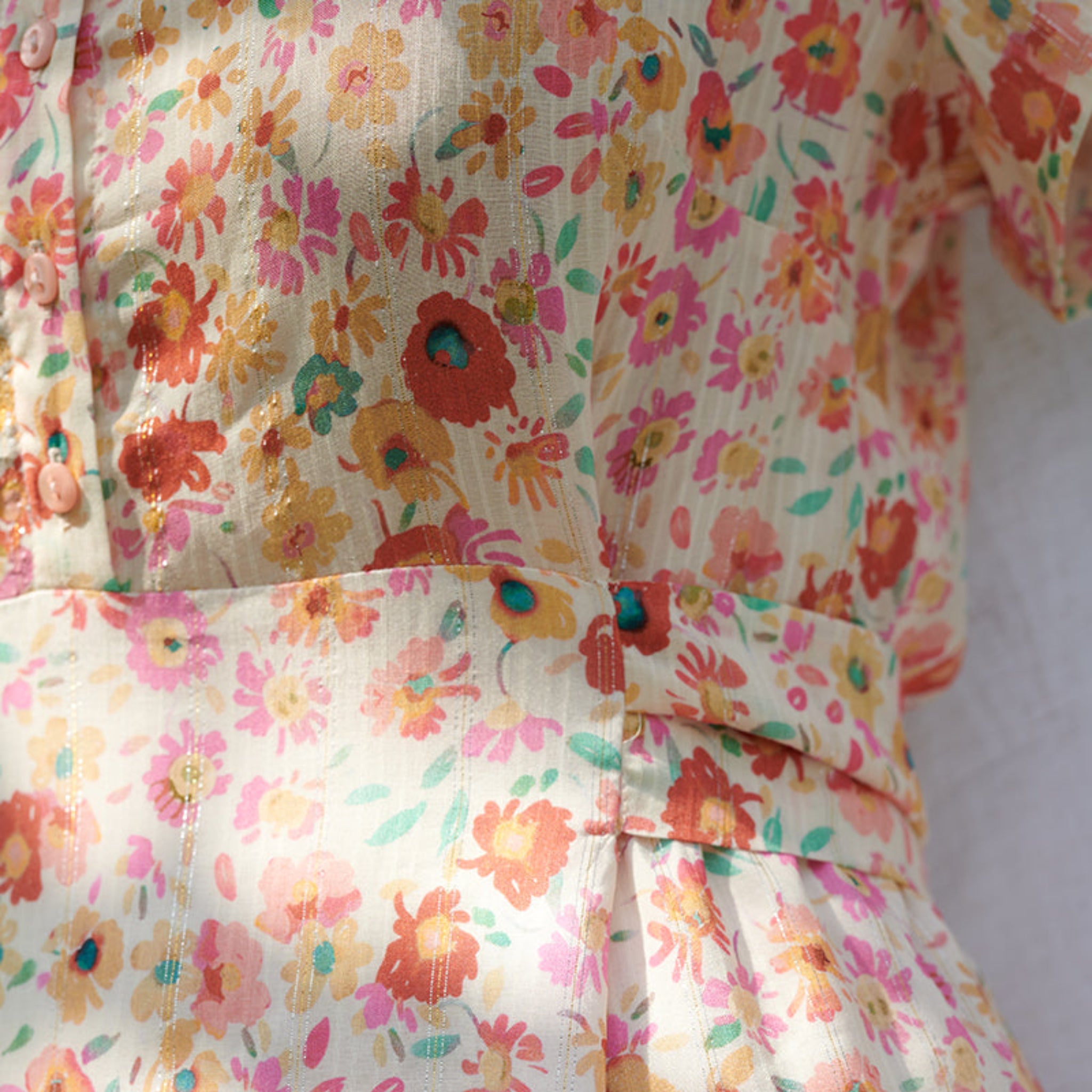 Nahaufnahme eines Kleides mit farbenfrohem Blumenmuster in Rot, Orange, Gelb und Grün auf hellem Stoff.