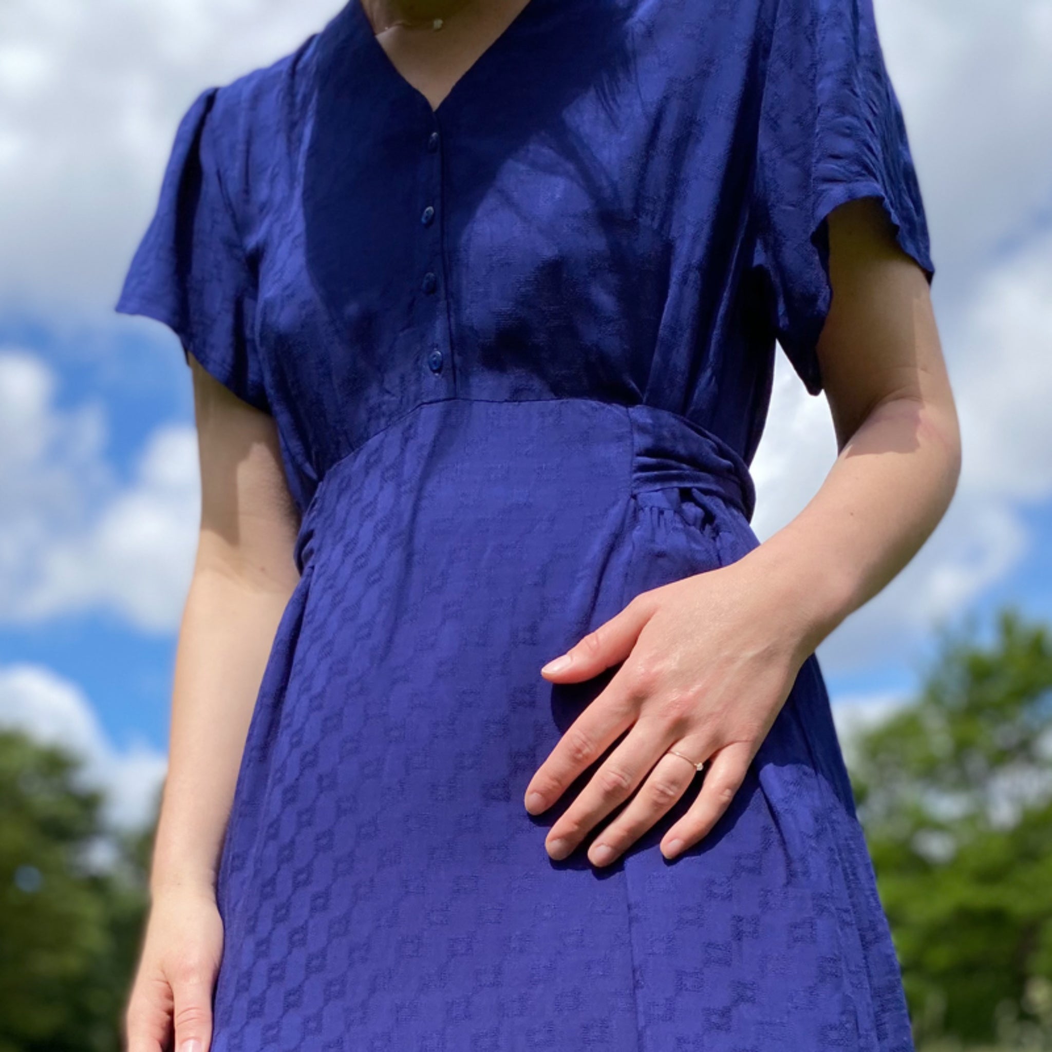 Person in a blue dress standing outside on a sunny day with a cloudy sky.