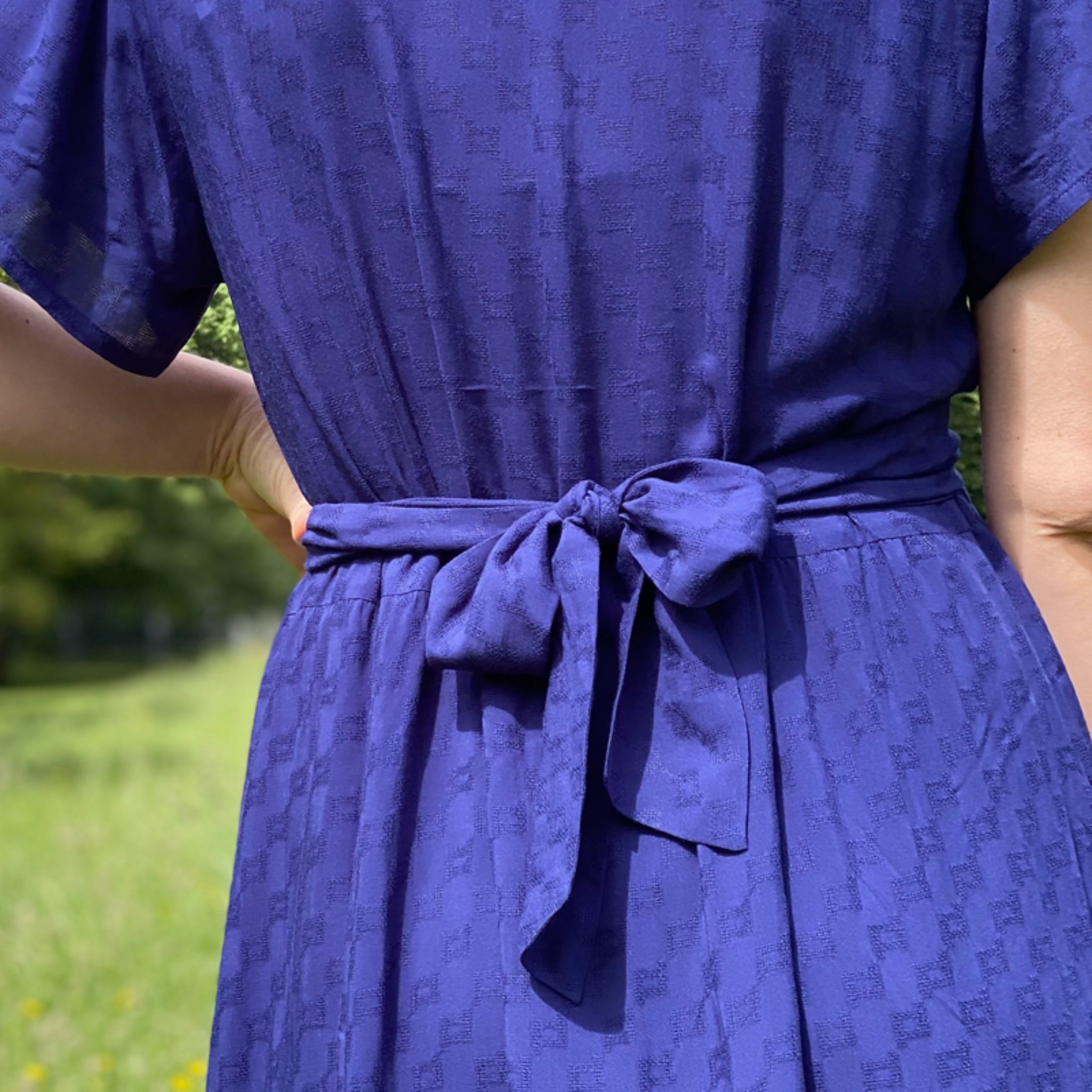 Eine Person von hinten, die ein blaues Kleid mit einer Schleife im Rückenbereich trägt.