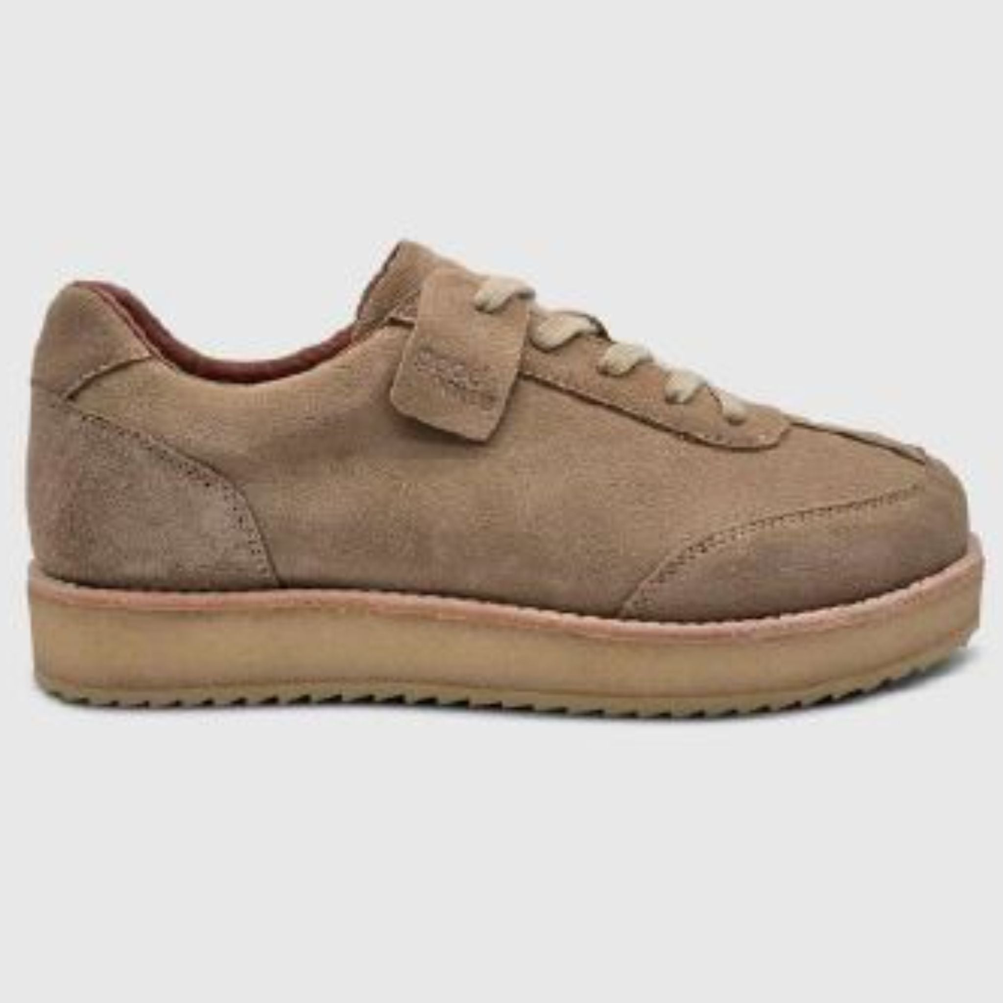 Hellbrauner Wildleder-Sneaker mit niedrigem Profil, Schnürung vorne und dicker beiger Sohle auf einfarbig grauem Hintergrund.