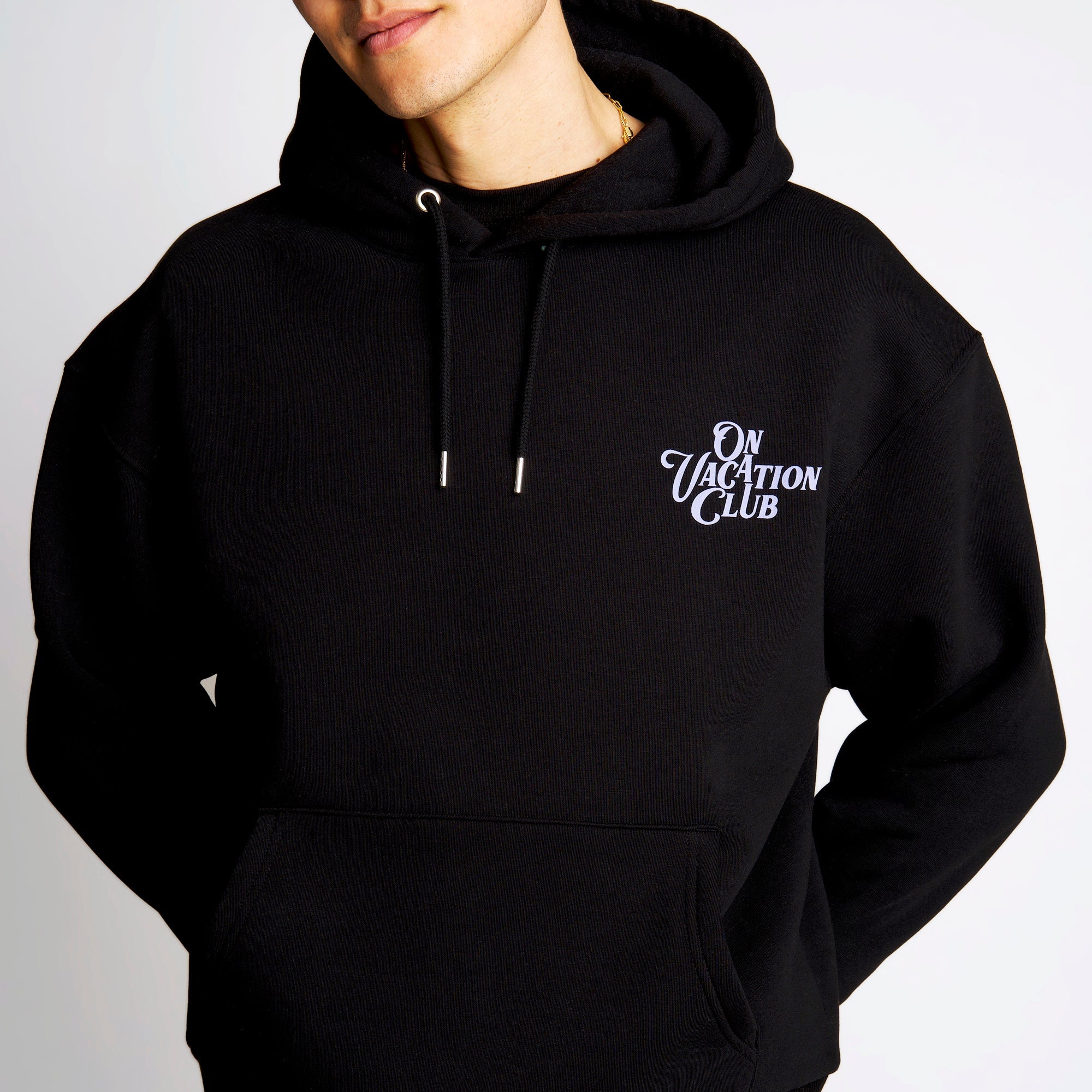 Person trägt einen schwarzen Hoodie mit dem Schriftzug "On Vacation Club" auf der Brust.