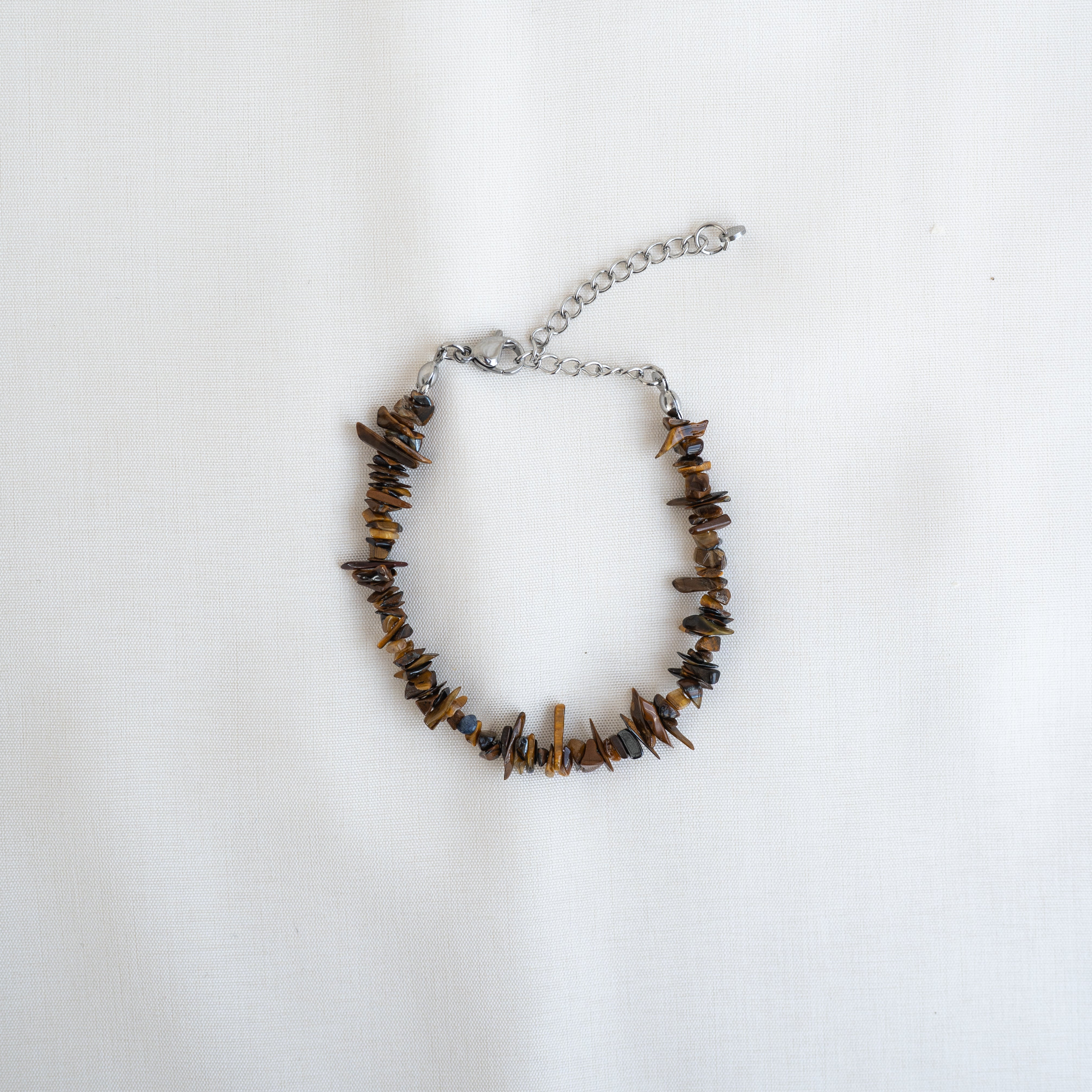 Ein Armband mit unregelmäßigen braunen Steinperlen und einem verstellbaren Silberkettenverschluss auf weißem Hintergrund.