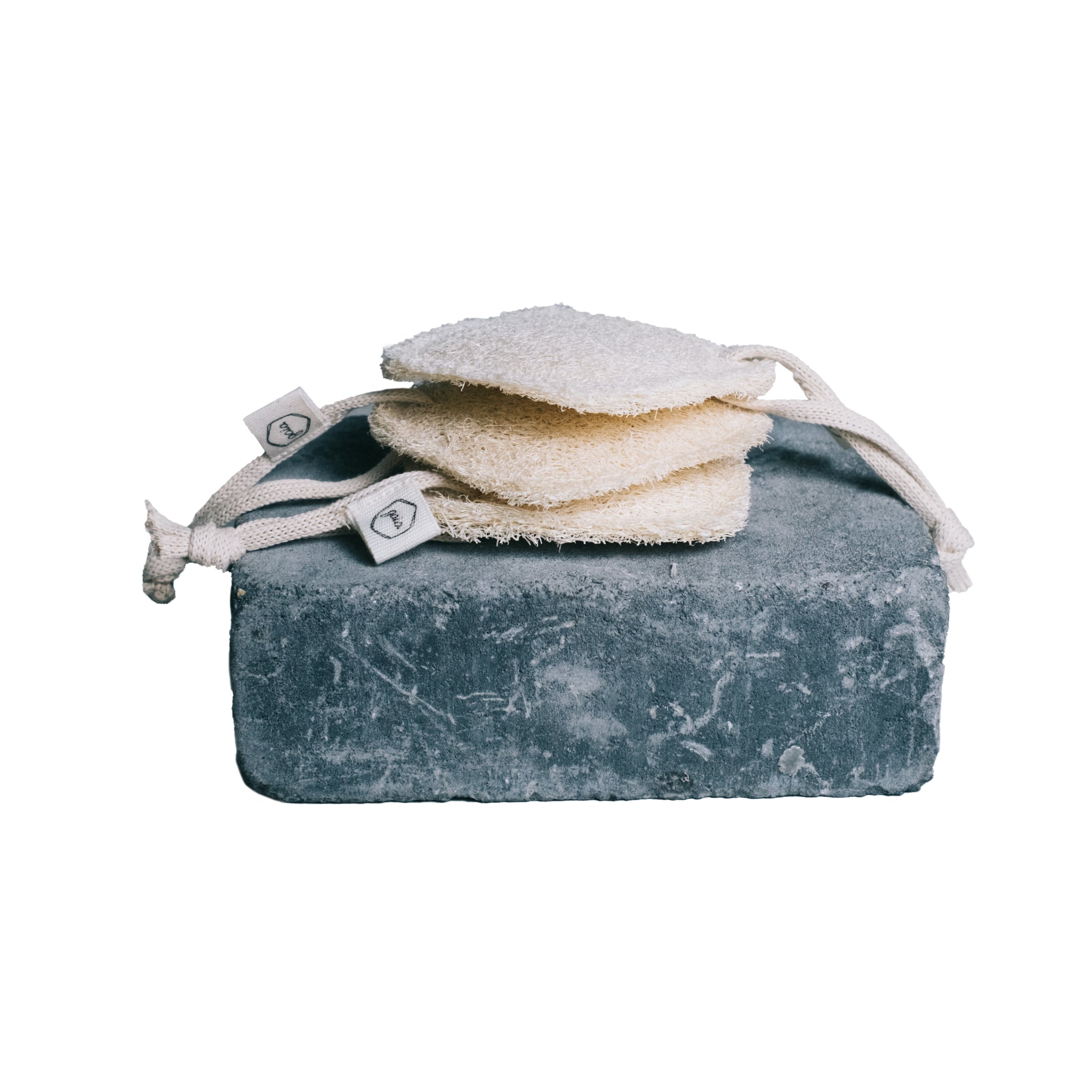 Ein Stapel aus vier natürlichen Schwämmen mit Kordeln liegt auf einem großen rechteckigen grauen Stein.