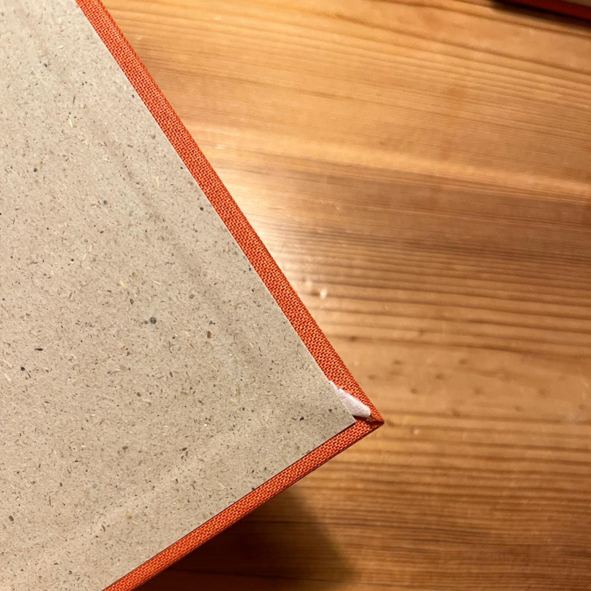 Ecke eines Buches mit orangefarbenem Einband und leicht abgenutzter Stelle, auf einem Holztisch liegend.