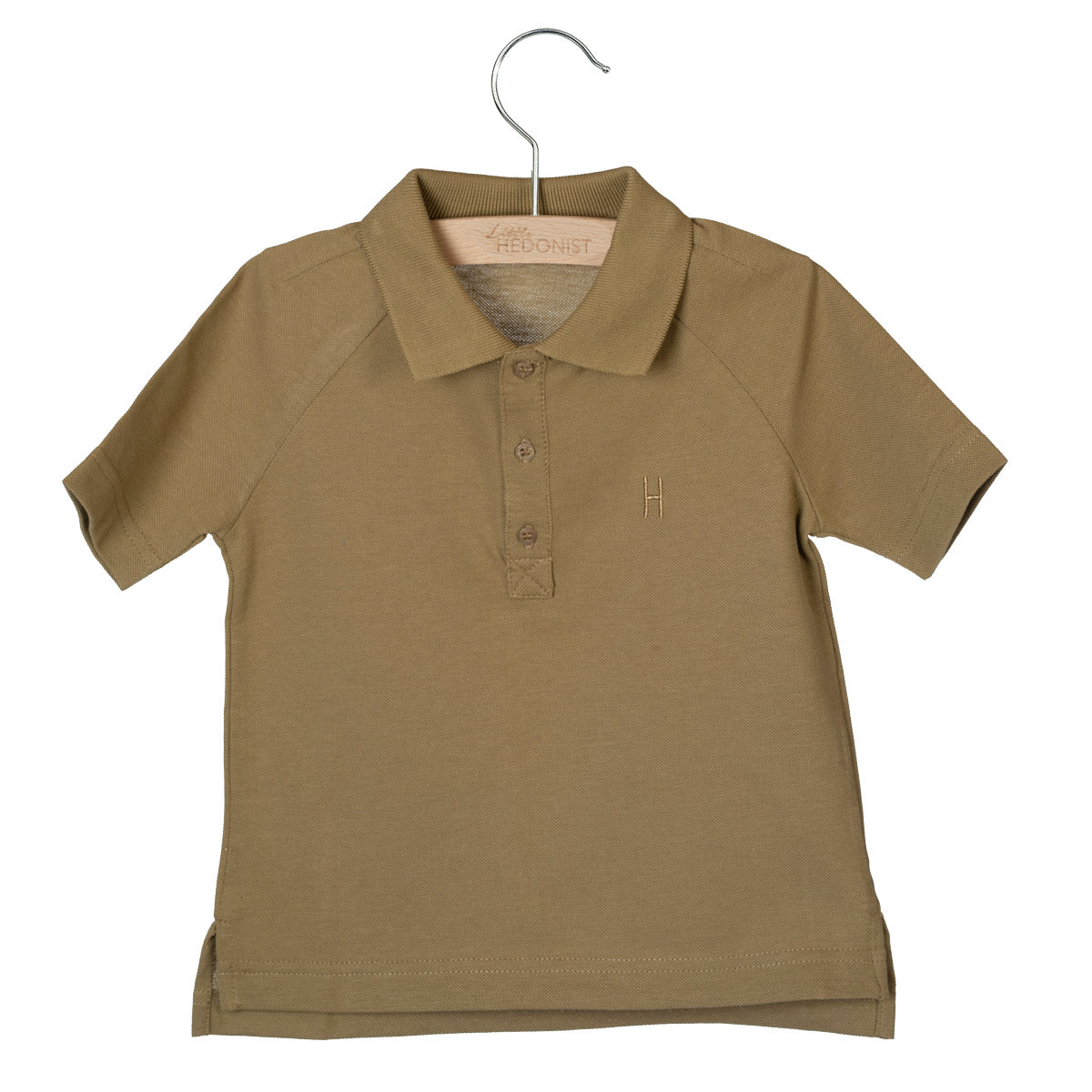 Ein kurzärmeliges, hellbraunes Poloshirt für Kinder ist auf einem Holzbügel ausgestellt. Das Hemd hat einen Kragen, drei Knöpfe, kurze Ärmel und ein kleines aufgenähtes H-Logo auf der linken Brust.