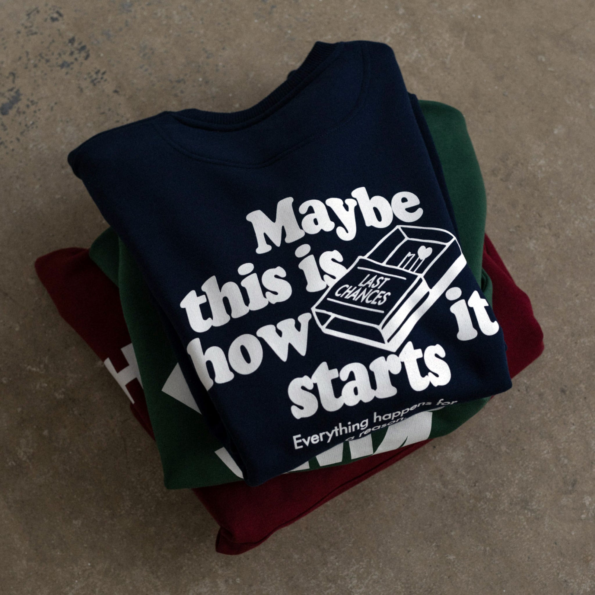 Drei gefaltete Pullover, oben mit dem Text: "Maybe this is how it starts" und einer gezeichneten Streichholzschachtel.
