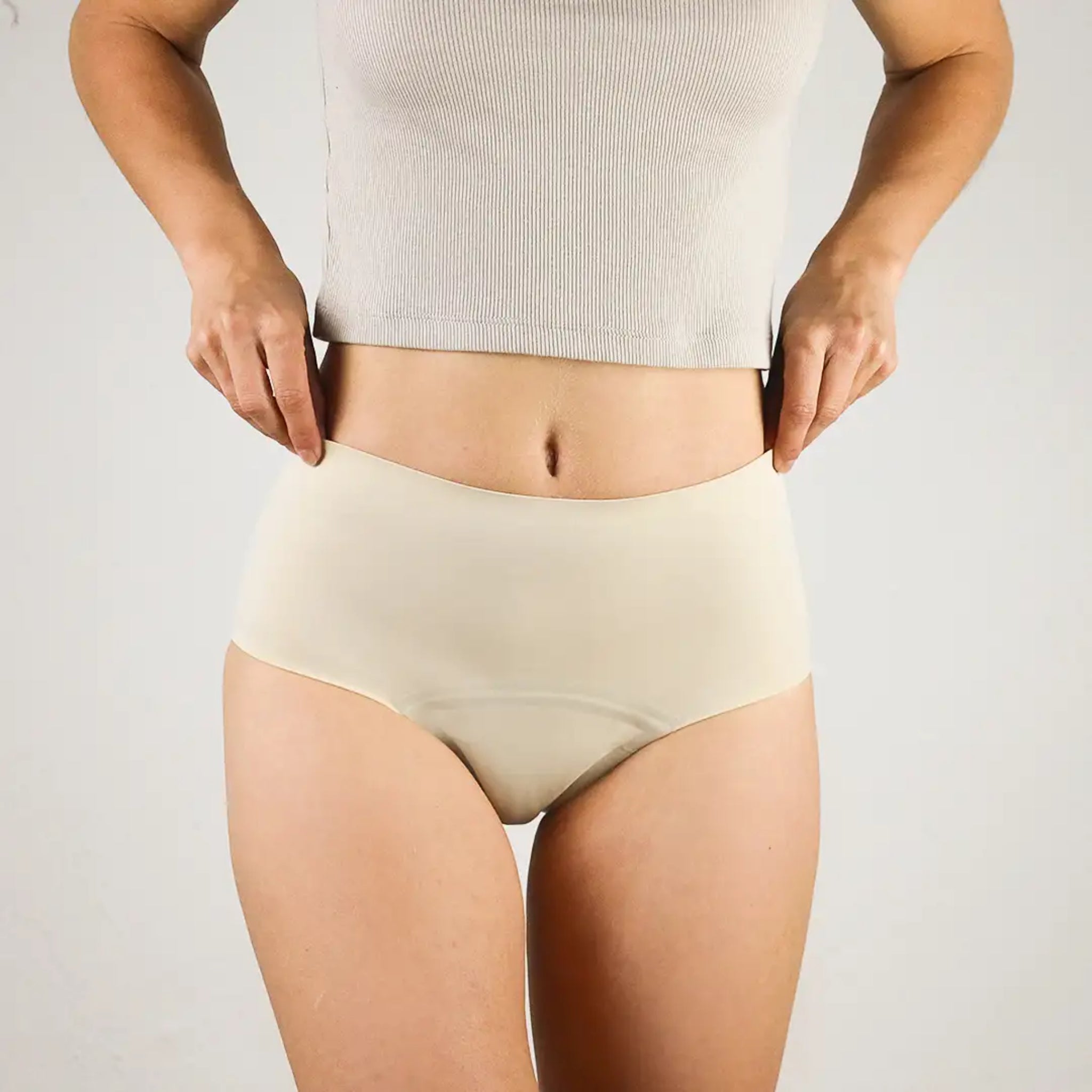 Person in beige Unterwäsche und grauem Oberteil, zeigt den elastischen Bund und die Passform vor neutralem Hintergrund.