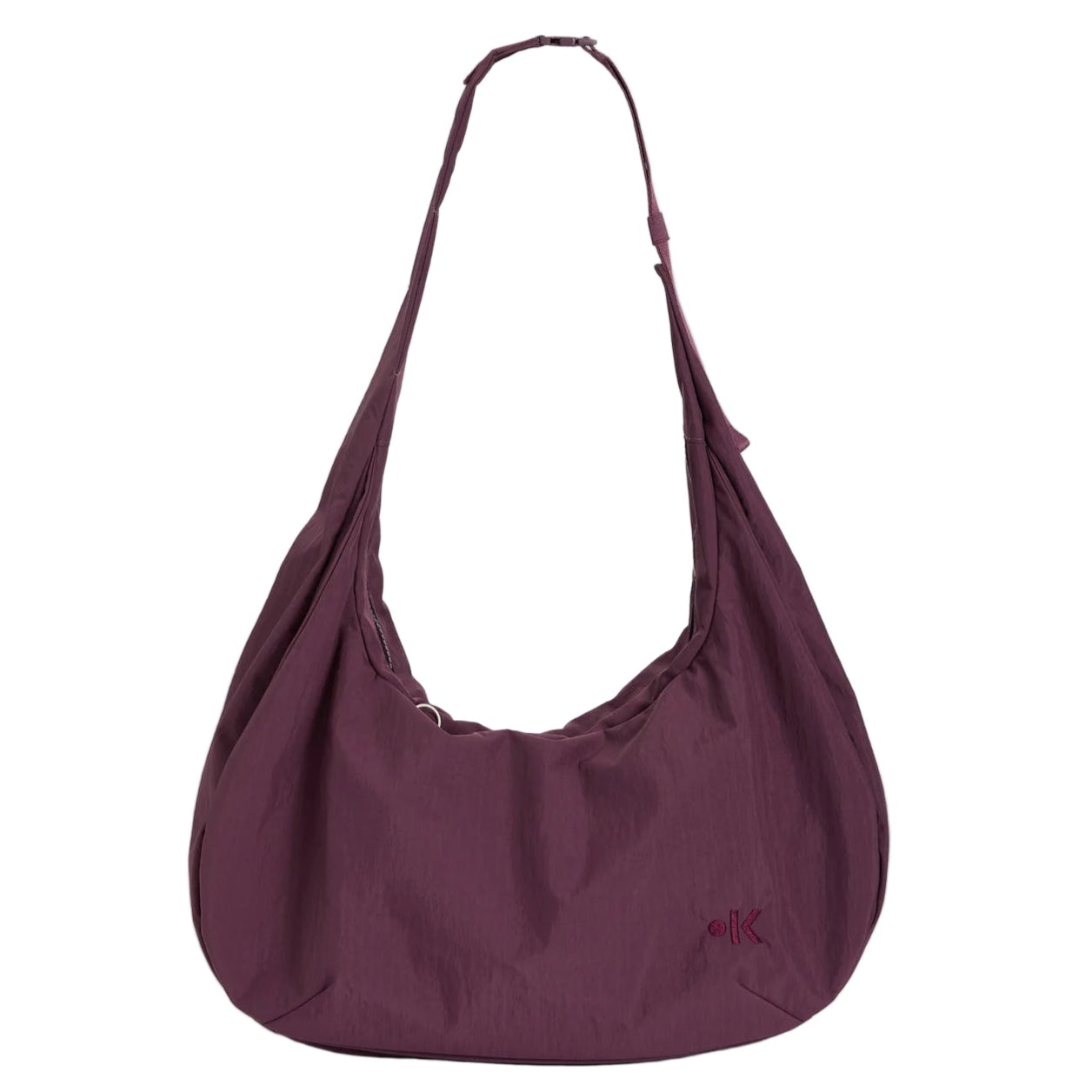 Eine große, weiche, dunkelviolette Umhängetasche mit einem einzigen breiten, oben leicht gerafften Riemen und einem kleinen Logo unten rechts auf der Vorderseite, das vor einem schlichten weißen Hintergrund steht.