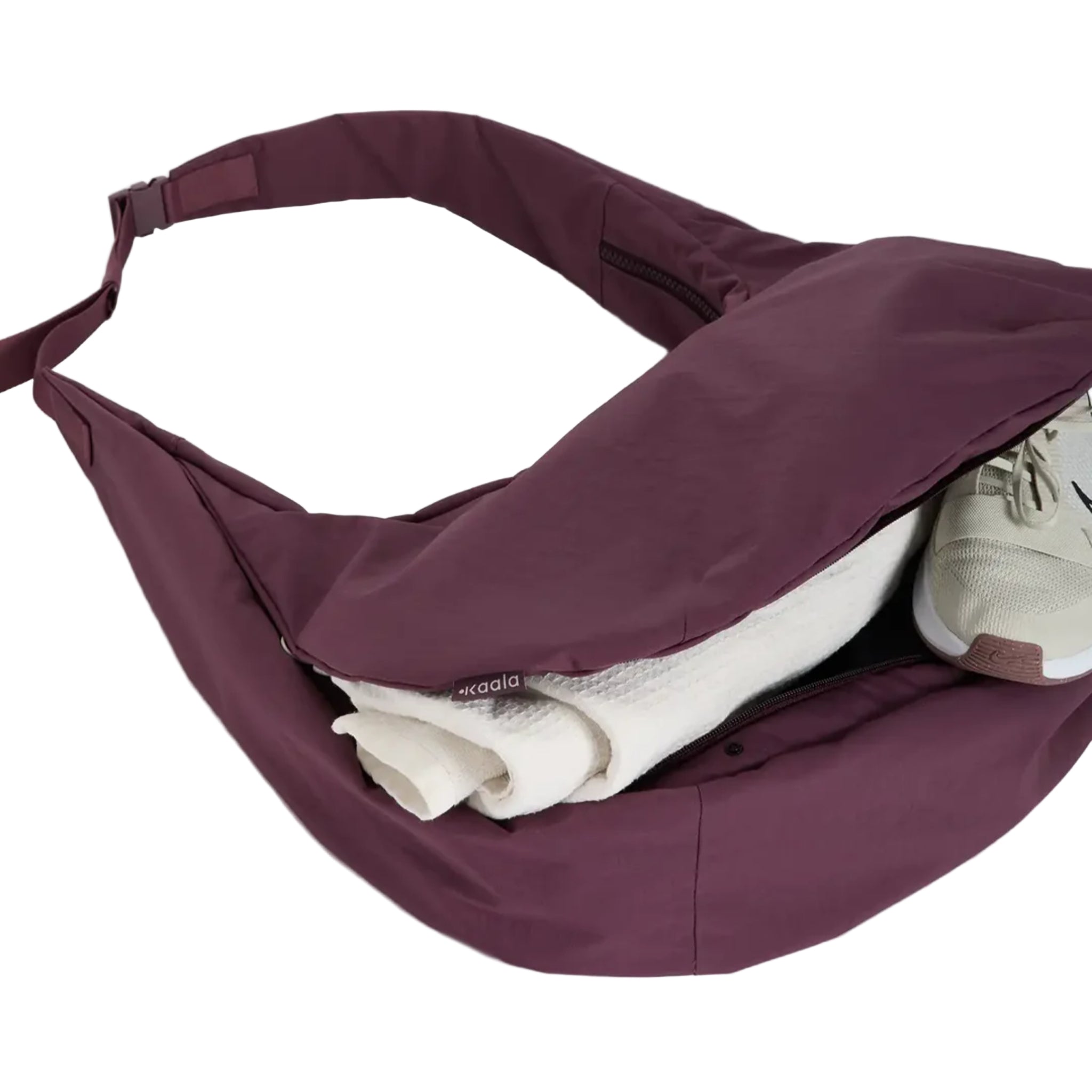 Eine große kastanienbraune Umhängetasche, deren Reißverschluss geöffnet ist und die ein aufgerolltes weißes Handtuch und einen weißen Turnschuh zeigt, der sich teilweise darin befindet, auf einem schlichten hellen Hintergrund.