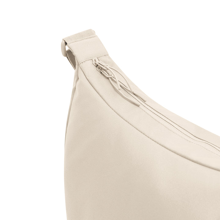 Nahaufnahme einer beigen Stofftasche mit sichtbarem Reißverschluss und Zuglasche auf einer Seite, die die Ecke und einen Teil des Riemens zeigt.