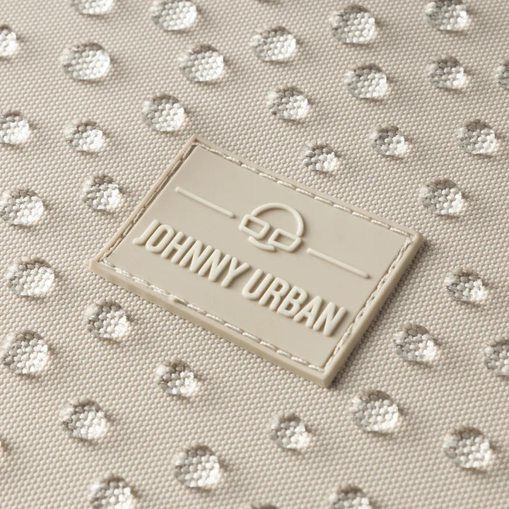 Nahaufnahme eines Stoffes mit einem Muster aus glänzenden, silbernen Punkten und einem beigen, rechteckigen Etikett mit der Aufschrift JOHNNY URBAN in erhabenen Buchstaben, das auf den Stoff genäht ist.