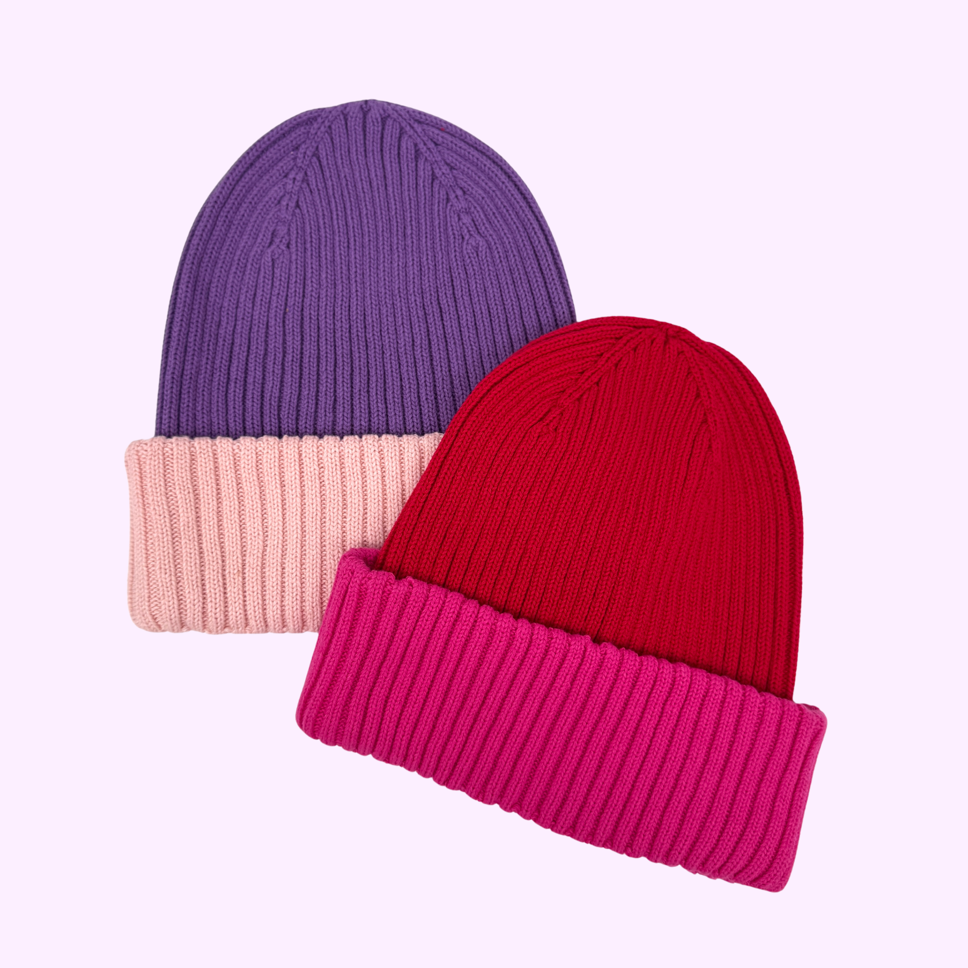 Zwei Rippenstrickmützen auf hellem Grund; eine ist lila mit einer rosa gefalteten Krempe, die andere ist rot mit einer leuchtend rosa gefalteten Krempe.