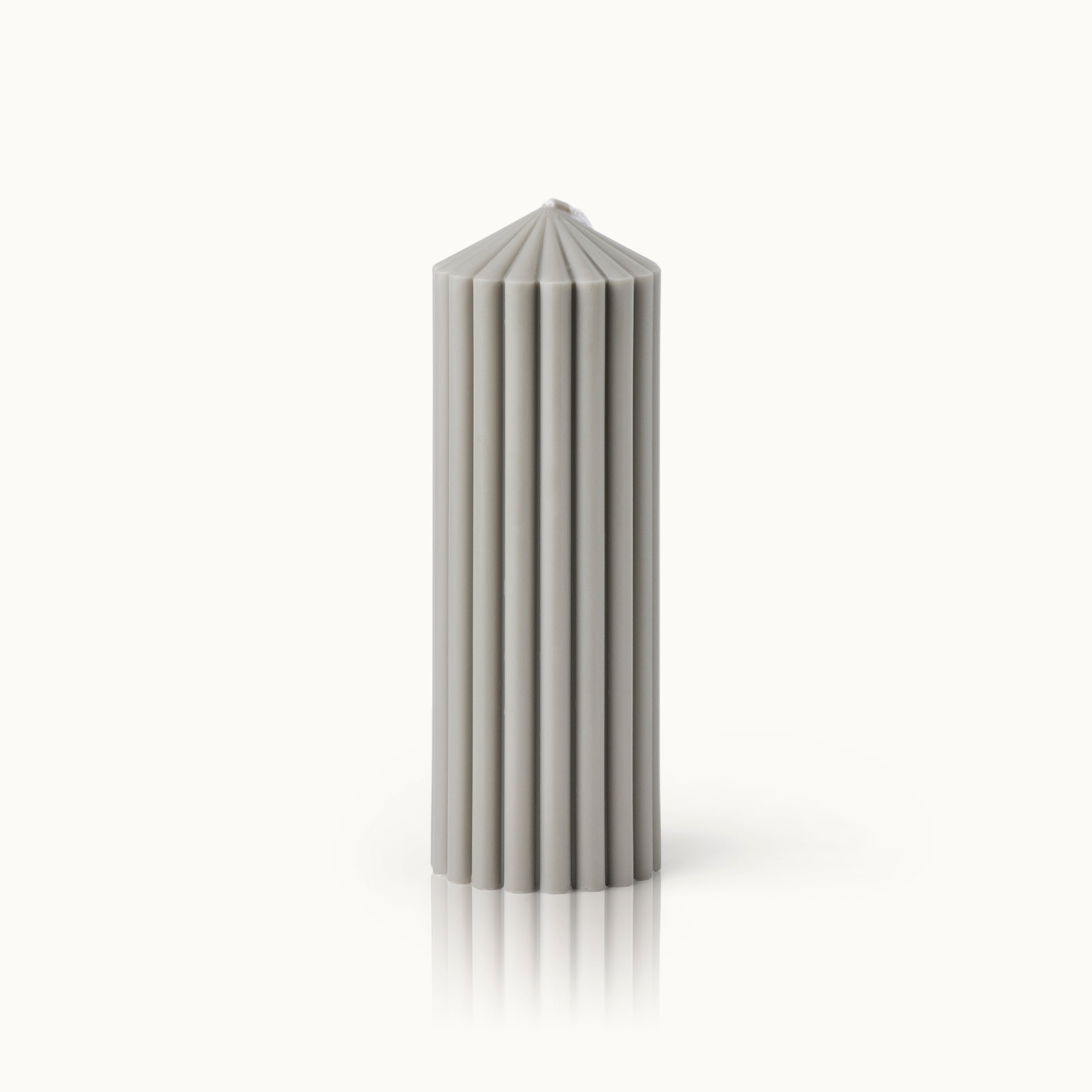 Eine hohe, zylindrische graue Kerze mit vertikalen Rillen und einer spitzen, facettierten Spitze, die aufrecht auf einem weißen Hintergrund steht.