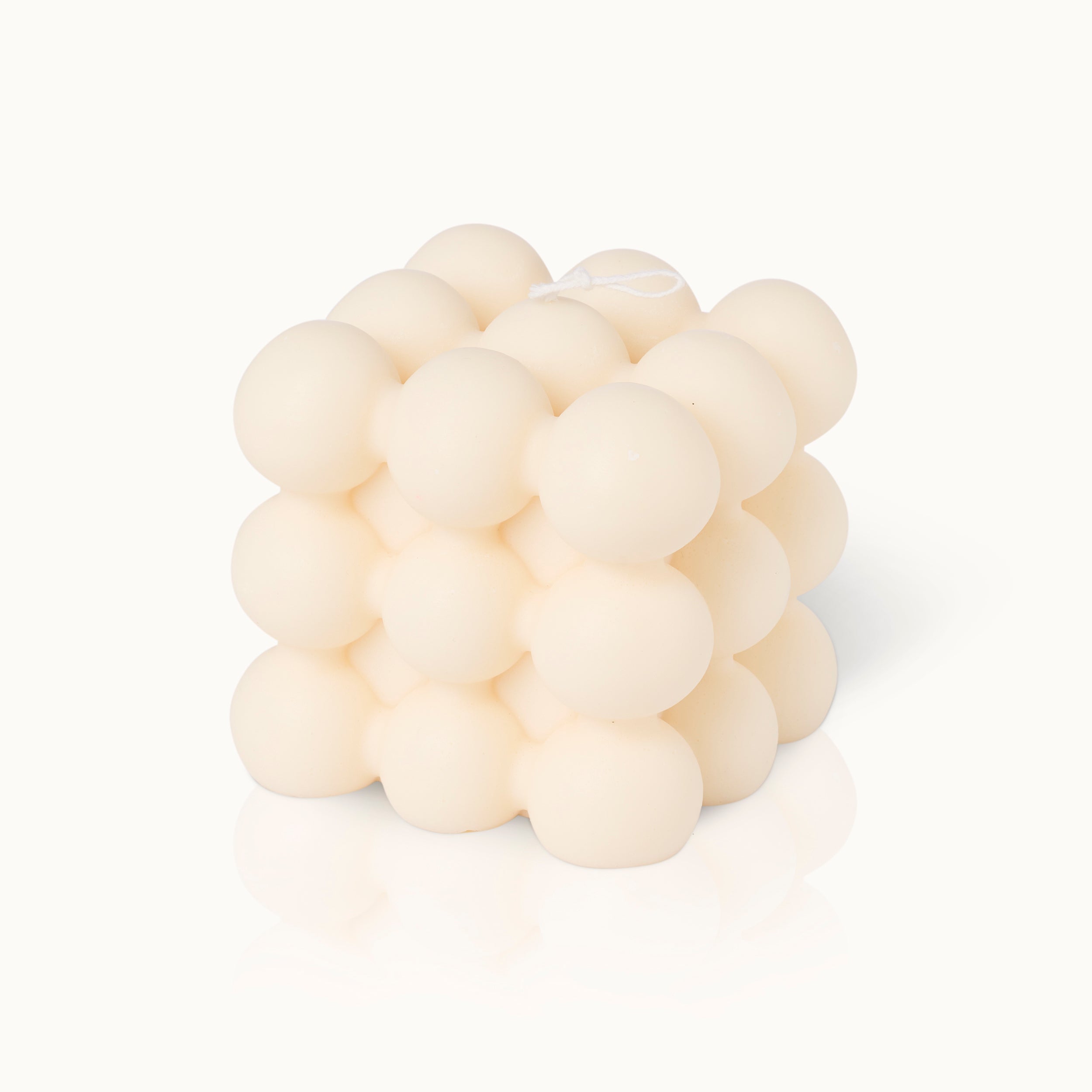 Eine cremefarbene, würfelförmige Kerze, bestehend aus Reihen von runden, blasenartigen Kugeln mit einem sichtbaren weißen Docht an der Spitze, vor einem schlichten weißen Hintergrund.