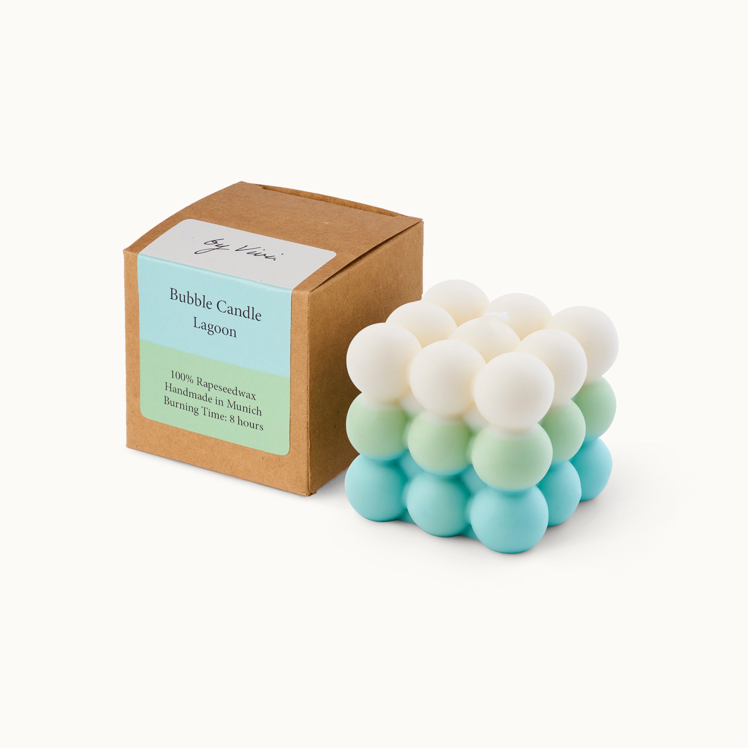 Eine pastellfarbene Seifenblasenkerze mit weißen, grünen und blauen Kugeln steht neben einer braunen Schachtel mit der Aufschrift Bubble Candle Lagoon. Auf dem Etikett steht, dass die Kerze zu 100 % aus Rapswachs besteht und 8 Stunden brennt.