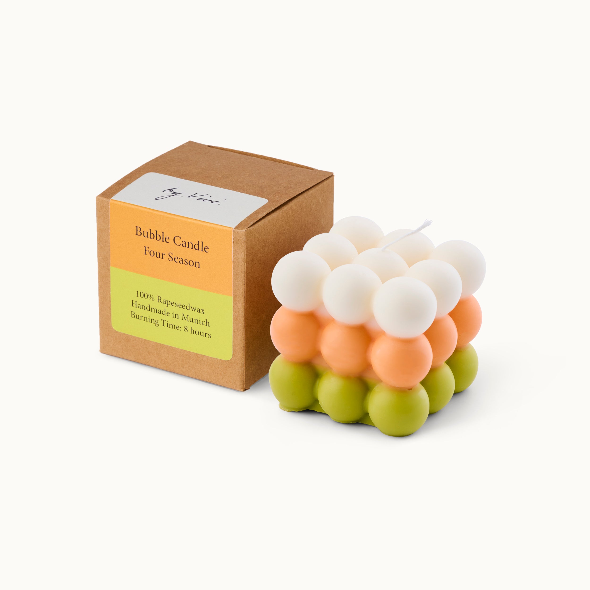 Eine bunte Bubble Candle mit grünen, orangefarbenen und weißen Kugeln neben einer braunen Schachtel mit der Aufschrift Bubble Candle Four Season; 100% Rapswachs, Handmade in Munich, Brenndauer 8 Stunden.