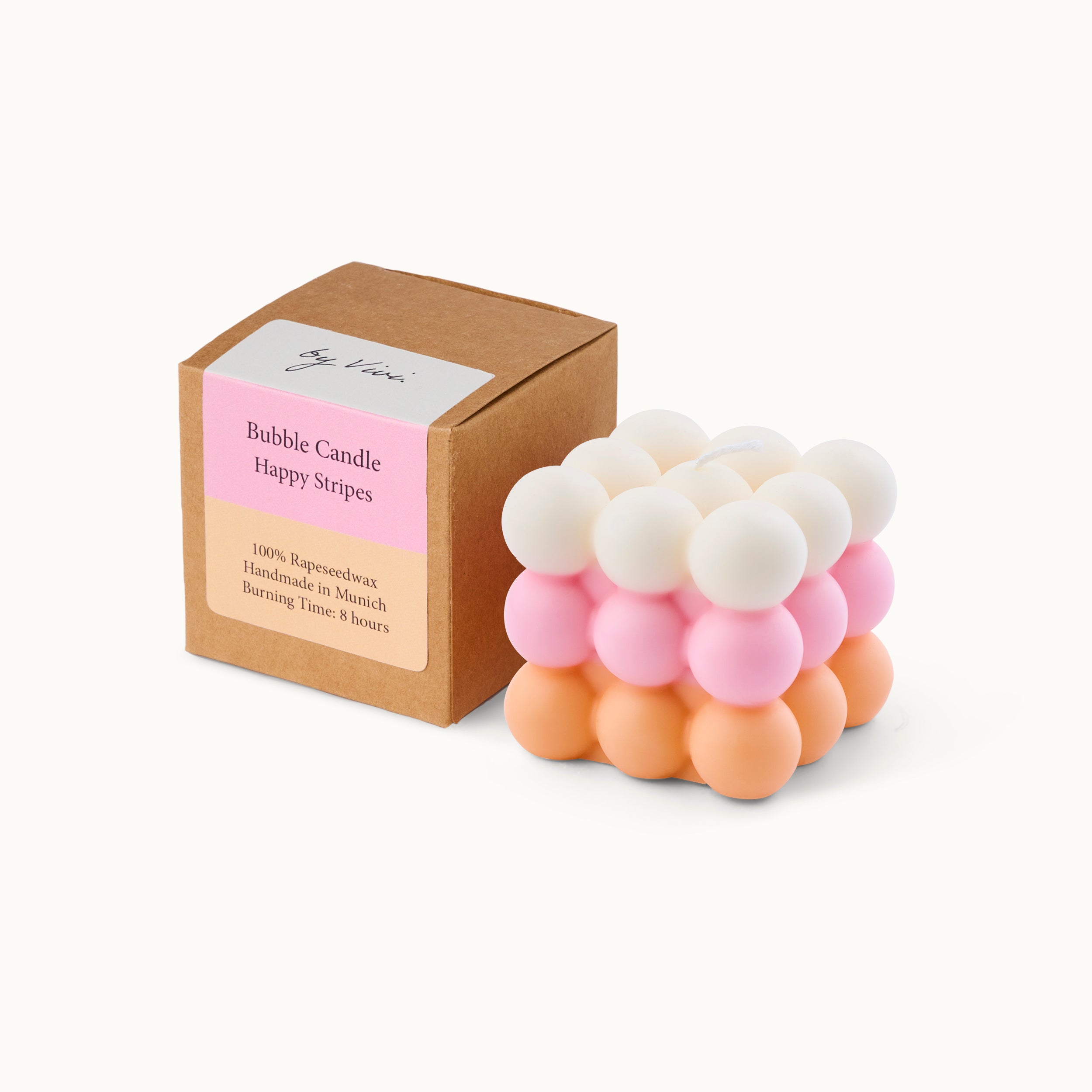 Eine pastellfarbene Bubble Candle mit weißen, rosafarbenen und pfirsichfarbenen Kugeln steht neben einer braunen Pappschachtel mit der Aufschrift Bubble Candle Happy Stripes. Auf der Schachtel steht auch, dass sie aus Rapswachs handgefertigt ist.