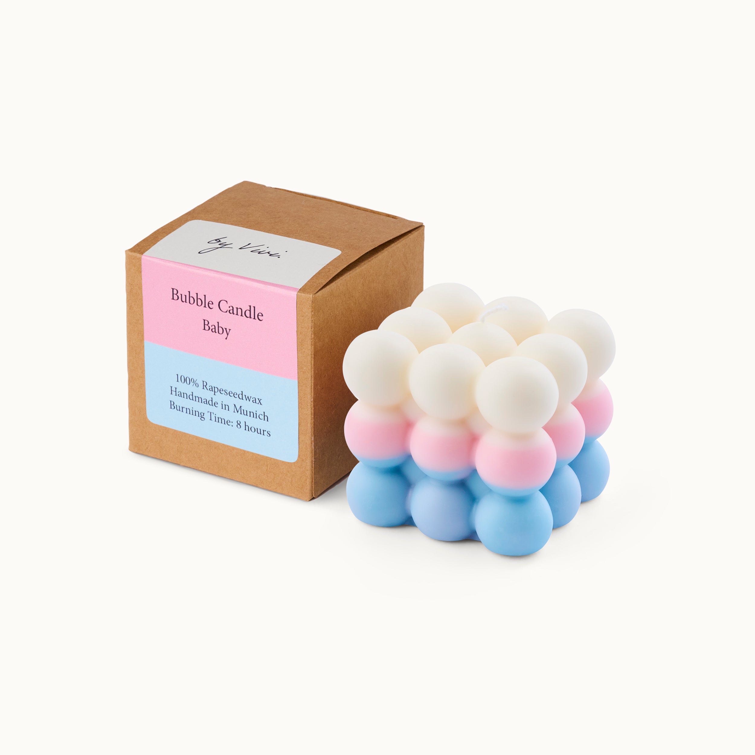 Eine pastellfarbene Seifenblasenkerze mit weißen, rosa und blauen Kugeln steht neben einer braunen Schachtel mit der Aufschrift Bubble Candle Baby und ähnlichen Pastellfarben auf dem Etikett.