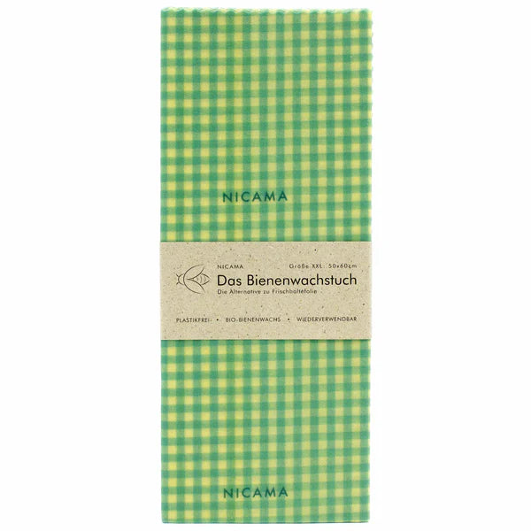Ein rechteckiges, grün-gelb kariertes Bienenwachstuch mit der Aufschrift NICAMA, verpackt in braunem Papier mit der Aufschrift "Das Bienenwachstuch" und Angaben auf Deutsch.