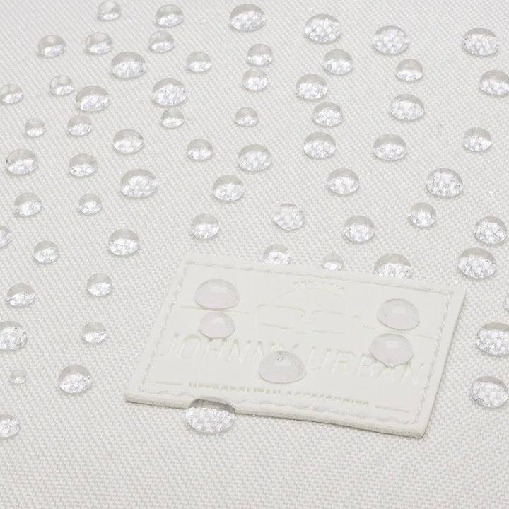 Nahaufnahme von Wassertropfen, die auf einer weißen, strukturierten Stoffoberfläche mit einem genähten rechteckigen Aufnäher abperlen. Der Stoff scheint wasserabweisend zu sein.