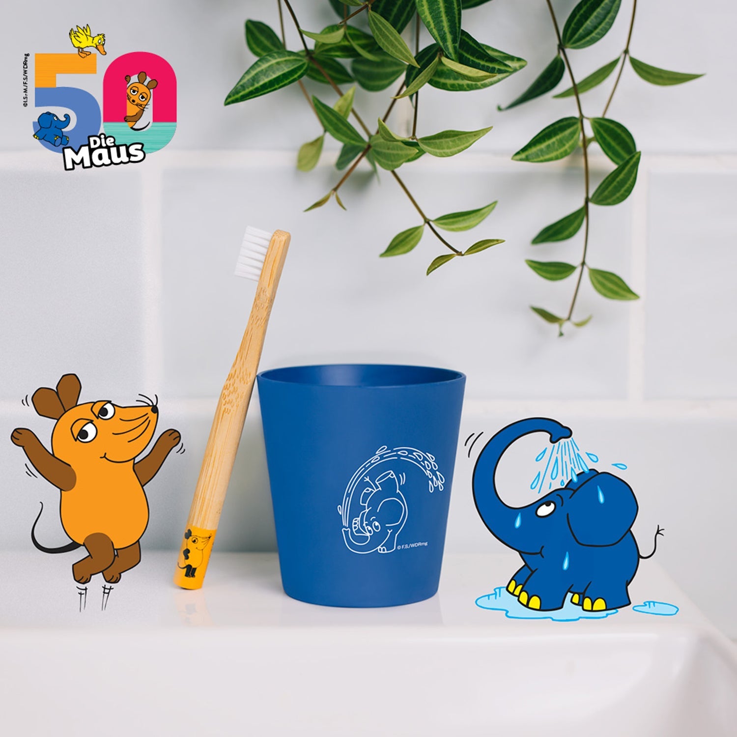Zahnbürste im blauen Becher mit Zeichnungen von einer Maus und einem Elefanten darunter, mit Pflanzen im Hintergrund.