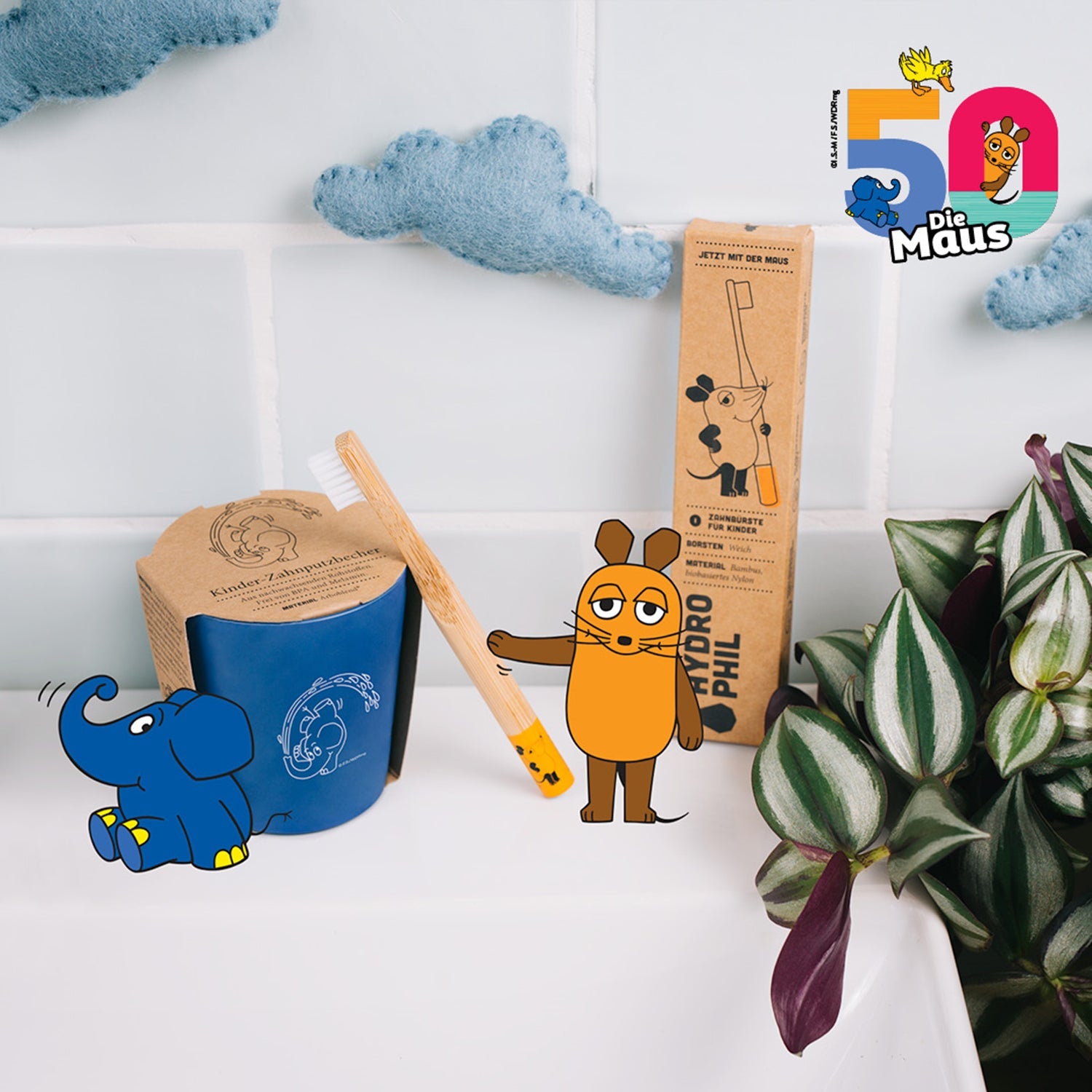 Zahnbürstenset mit der Maus und dem Elefanten in einem Badezimmer mit Pflanzen und Wolken-Dekoration.