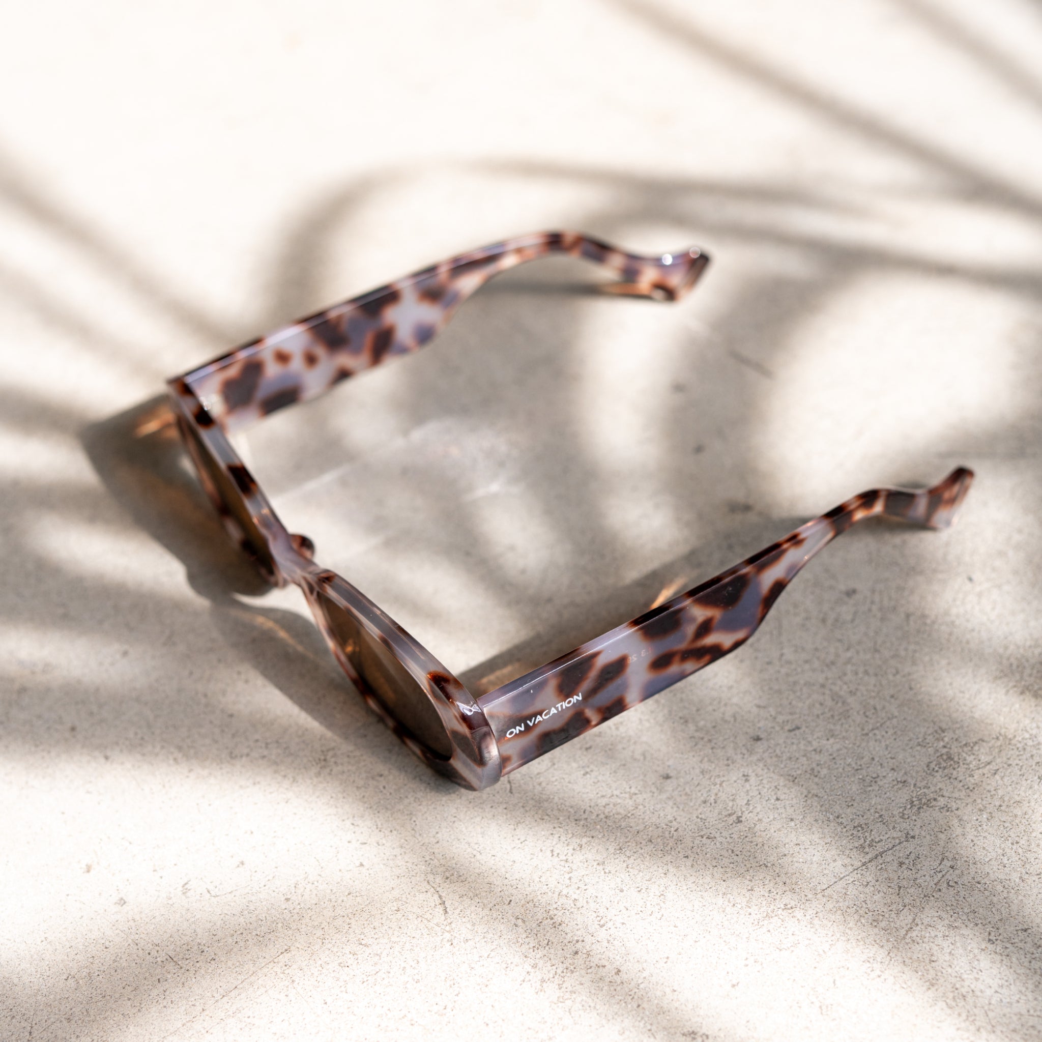 Braune Schildpatt-Sonnenbrille mit geradlinigem Rahmen liegt auf einem hellen, von Schatten durchzogenen Untergrund.