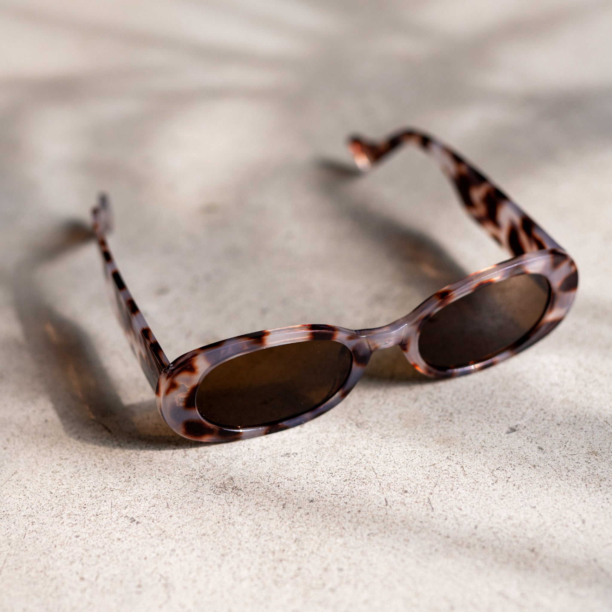 Braune Sonnenbrille mit Schildpattmuster auf einem hellen Untergrund, sanft beschattet.