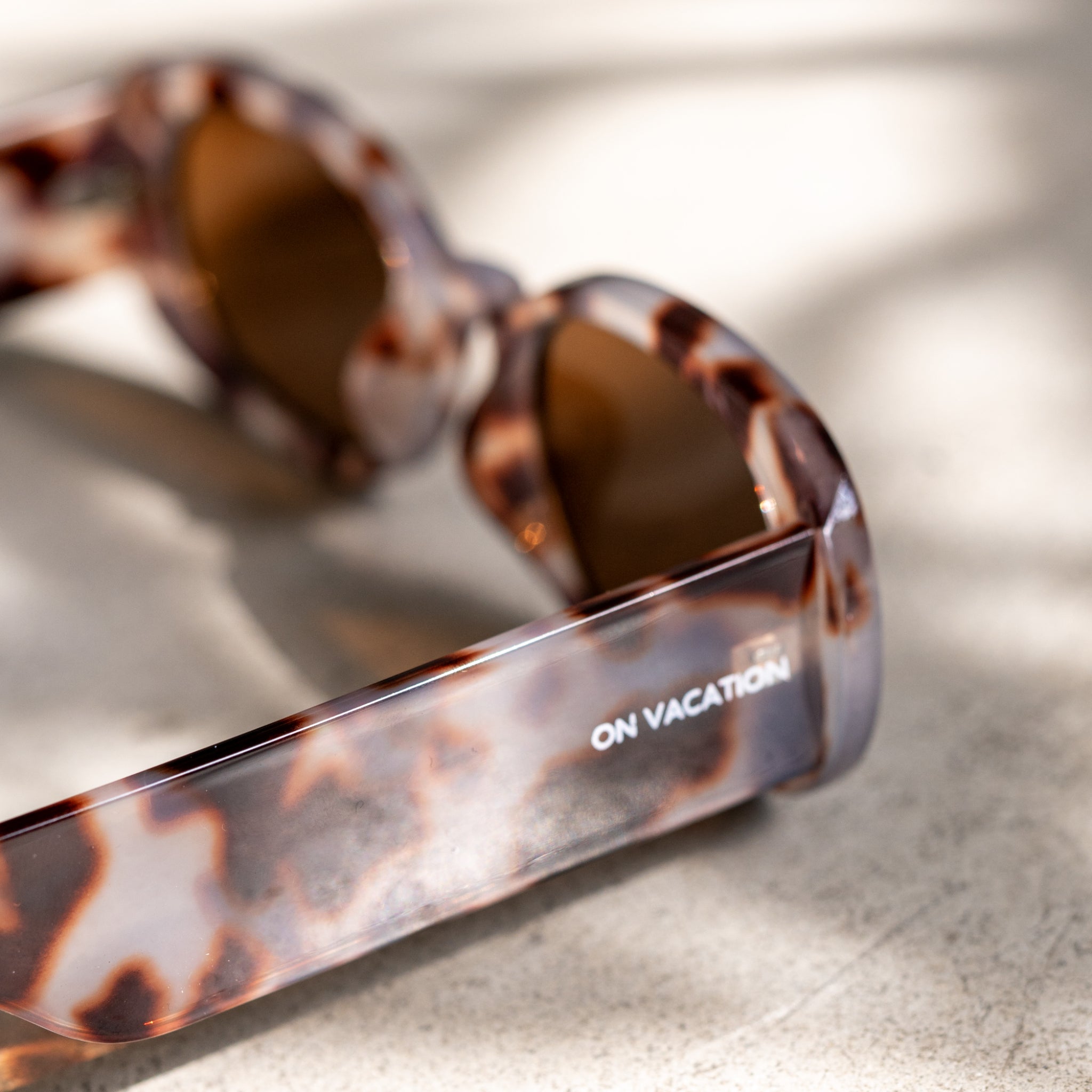Nahaufnahme einer Sonnenbrille mit Schildpattmuster und der Aufschrift "ON VACATION" auf einem der Bügel.