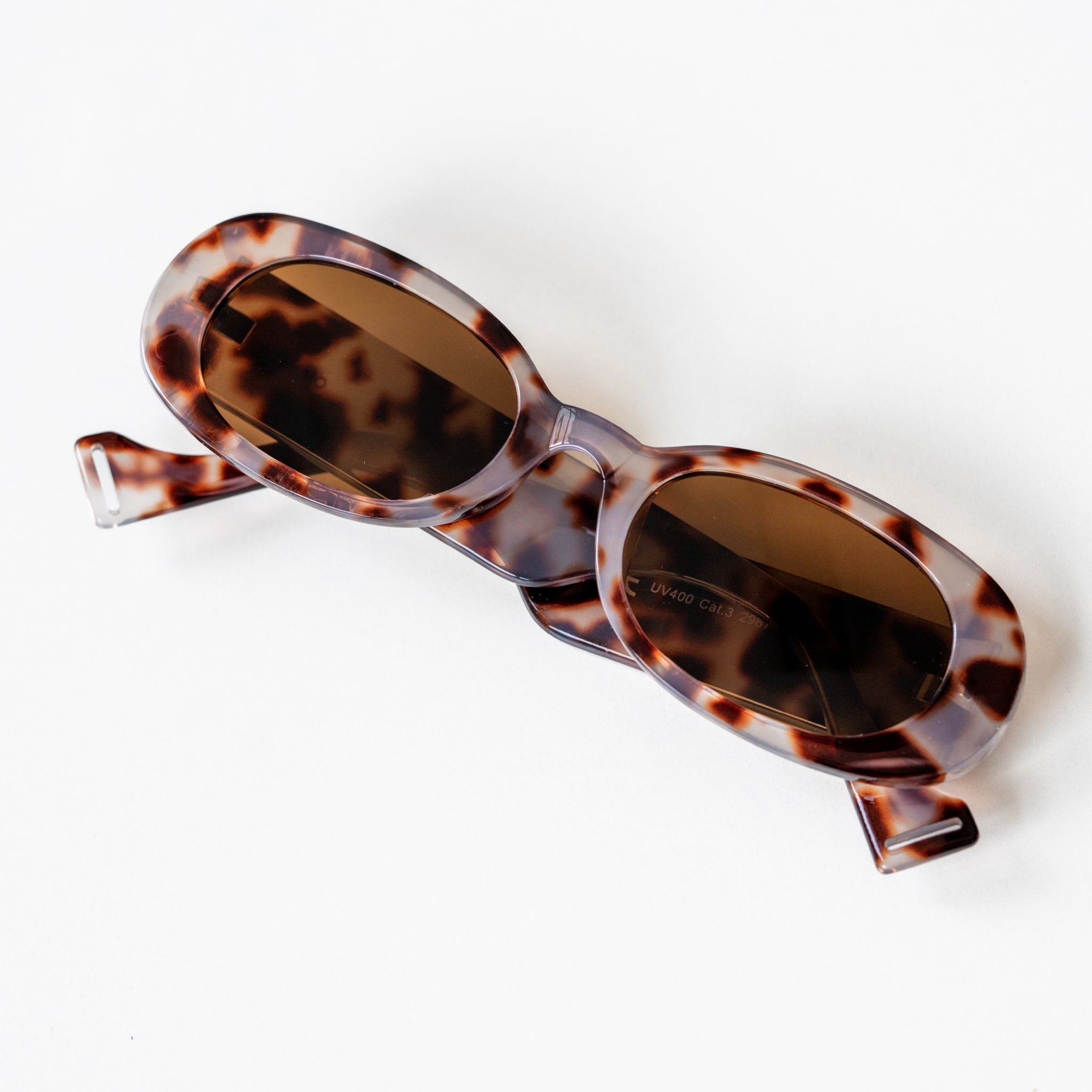 Sonnenbrille mit ovalen Gläsern und einem marmorierten braun-weißen Gestell auf weißem Hintergrund.