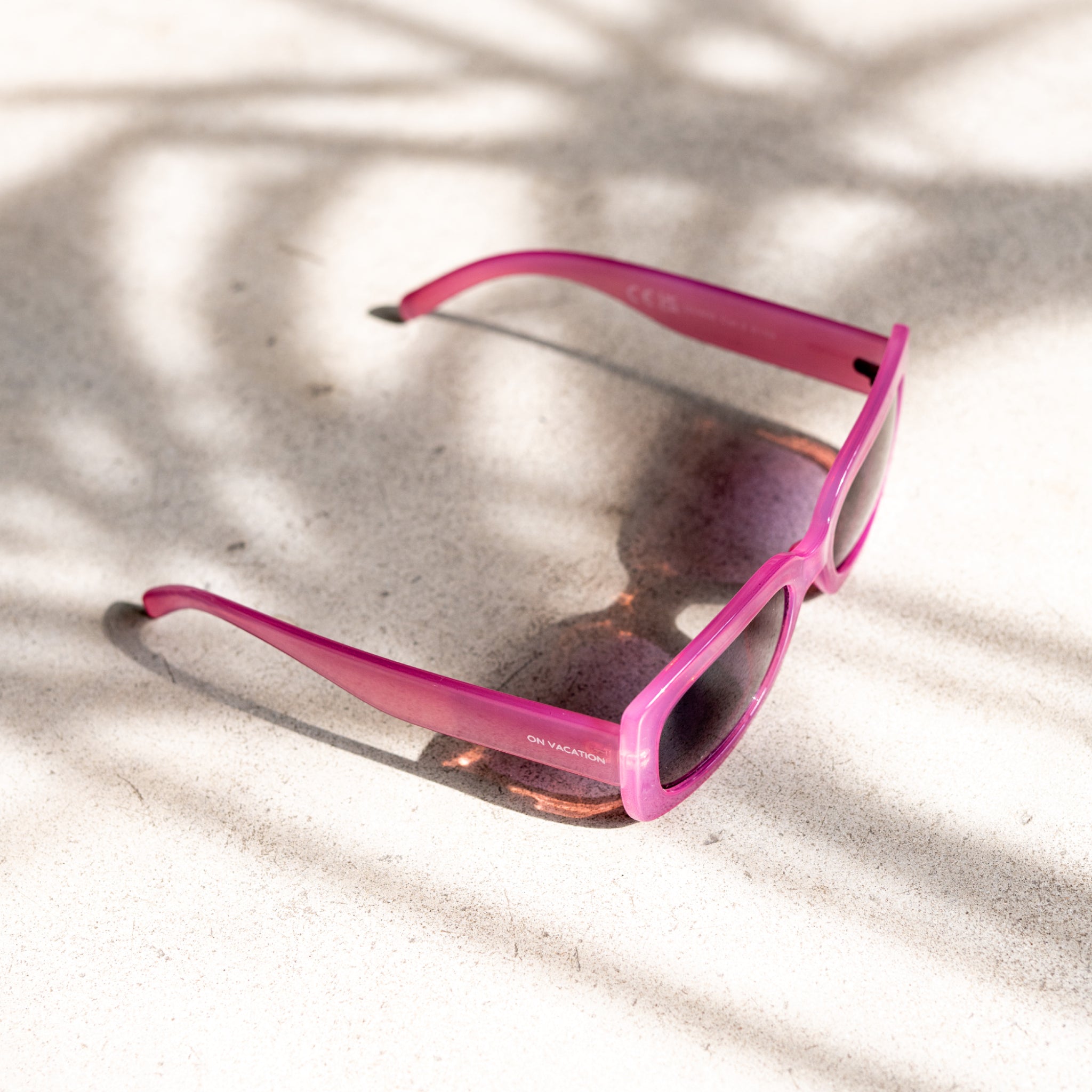 Rosa Sonnenbrille mit polarisiertem Sonnenlicht und Schattenmustern, liegt auf einer hellen Oberfläche.