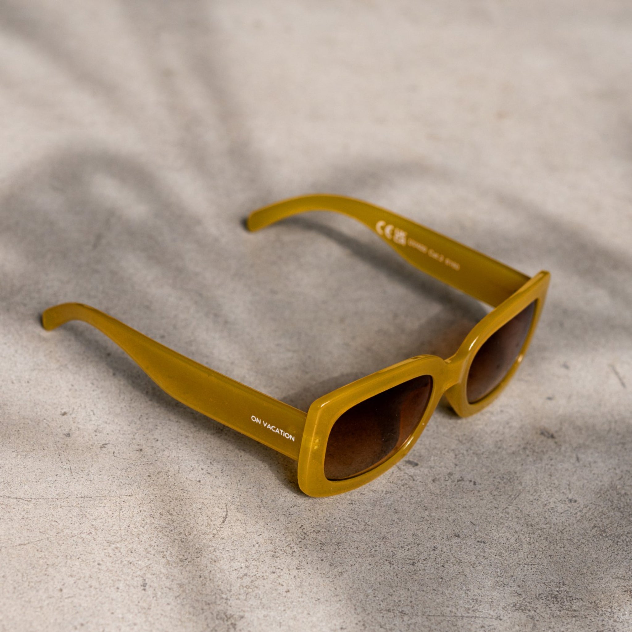 Gelbe Sonnenbrille liegt auf einem hellen Untergrund mit sanften Schatten im Hintergrund.