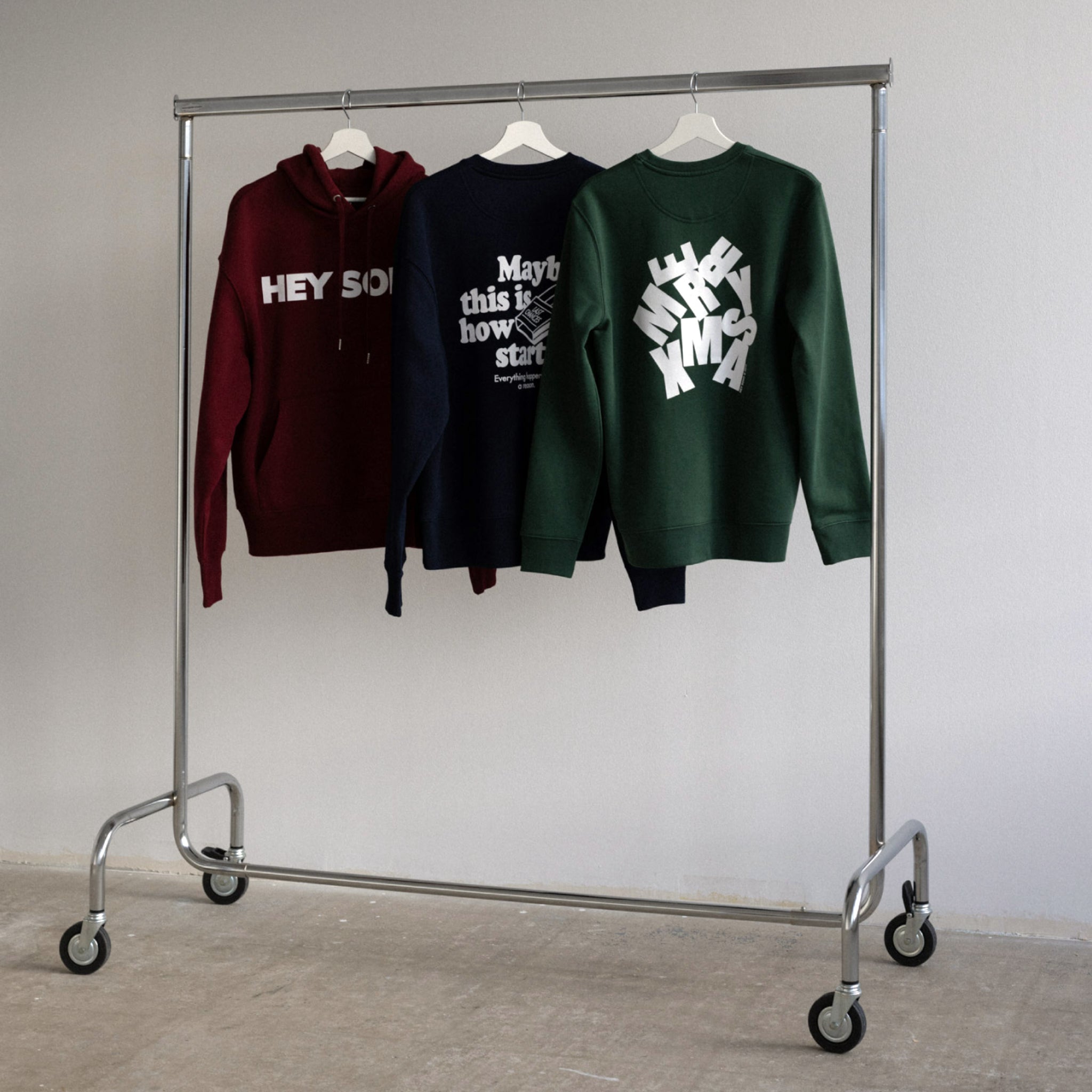 Drei Pullover mit Schriftzügen hängen auf Kleiderbügeln an einem Metallständer.