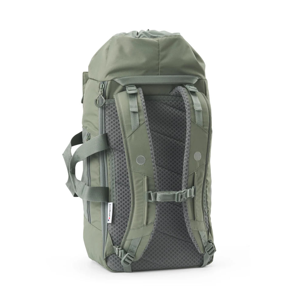 Ein grüner Rucksack mit gepolsterten, verstellbaren Schulterriemen, seitlichen Griffen, Netzrückwand und Reißverschlussfächern steht aufrecht auf weißem Hintergrund.