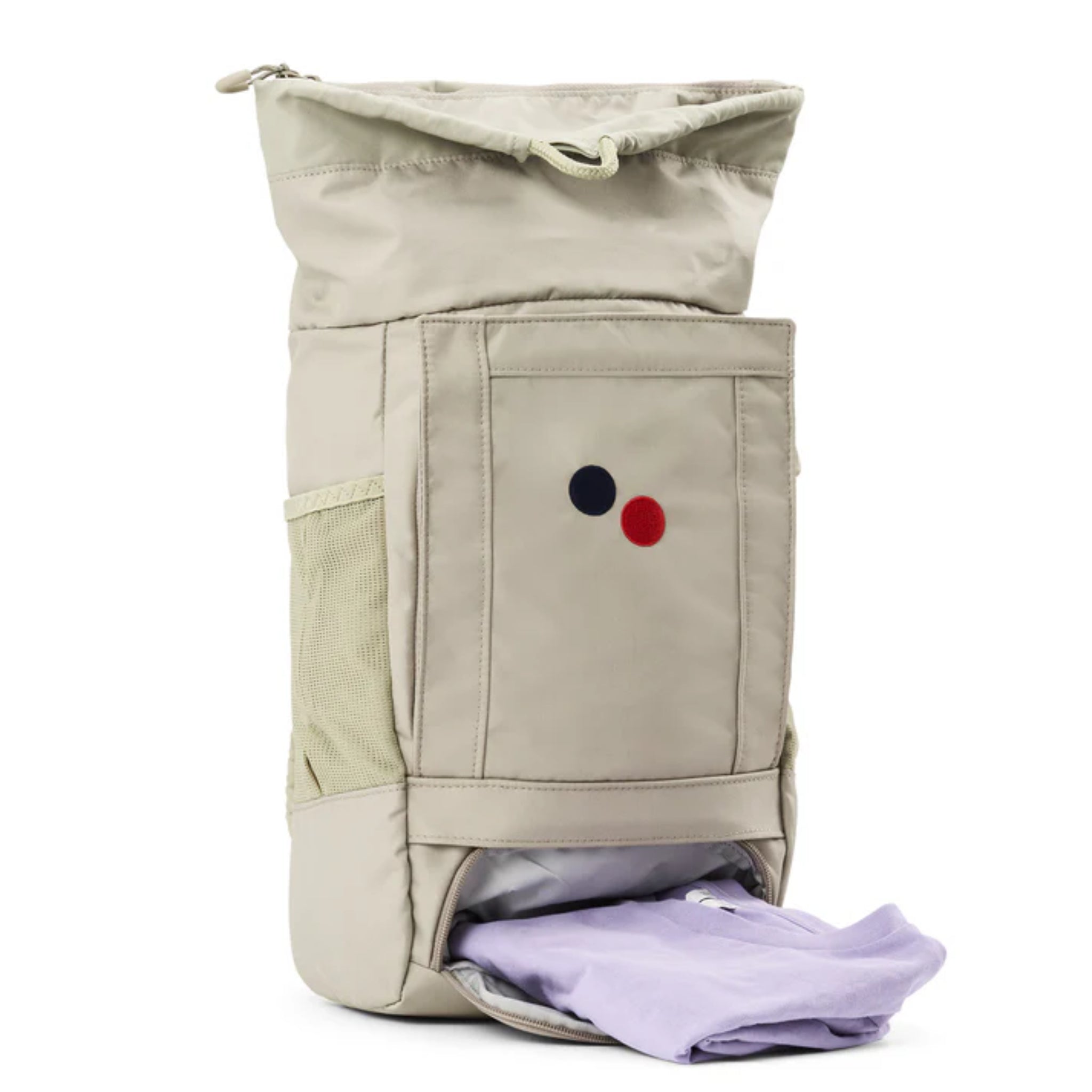 Ein beiger Rucksack mit einer Vordertasche, einer Netztasche an der Seite und zwei kleinen runden Aufnähern (einer rot, einer marineblau). Das untere Fach ist offen und offenbart ein gefaltetes lavendelfarbenes Hemd, das teilweise herausgezogen ist.