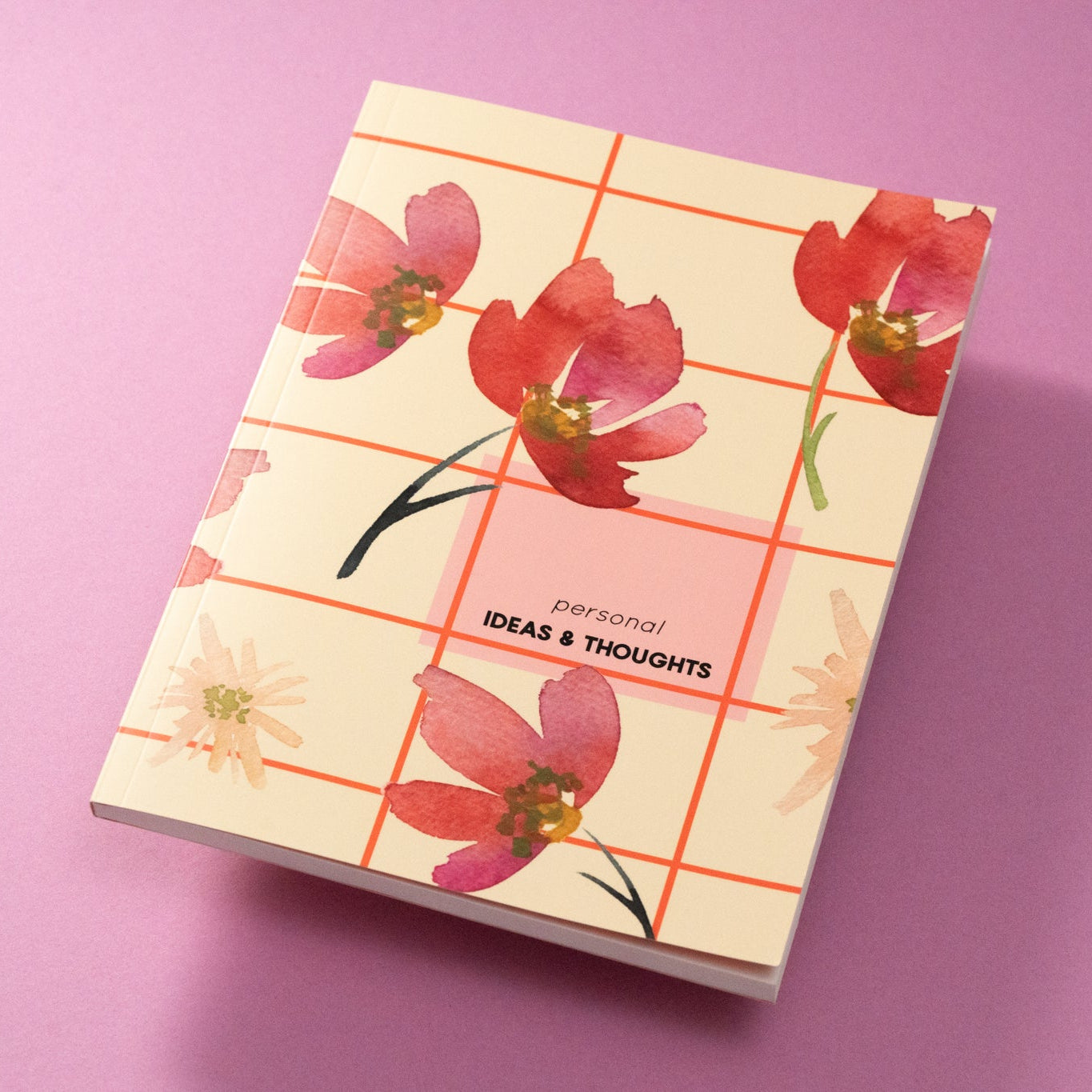 Ein Notizbuch mit cremefarbenem Einband zeigt rote und rosafarbene Aquarellblumen und ein Gittermuster mit der Aufschrift "Personal IDEAS & THOUGHTS" auf einer rosafarbenen Fläche.
