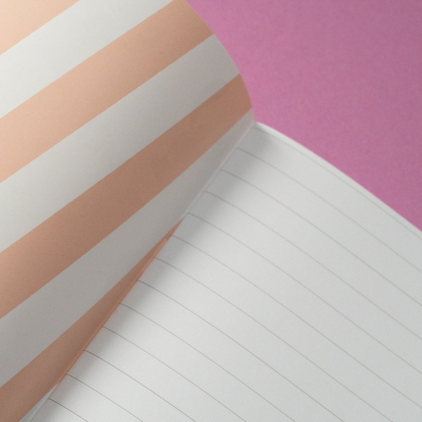 Nahaufnahme eines aufgeschlagenen Notizbuchs mit weiß linierten Seiten und einem Einband mit beigen und weißen Diagonalstreifen vor einem rosa Hintergrund.
