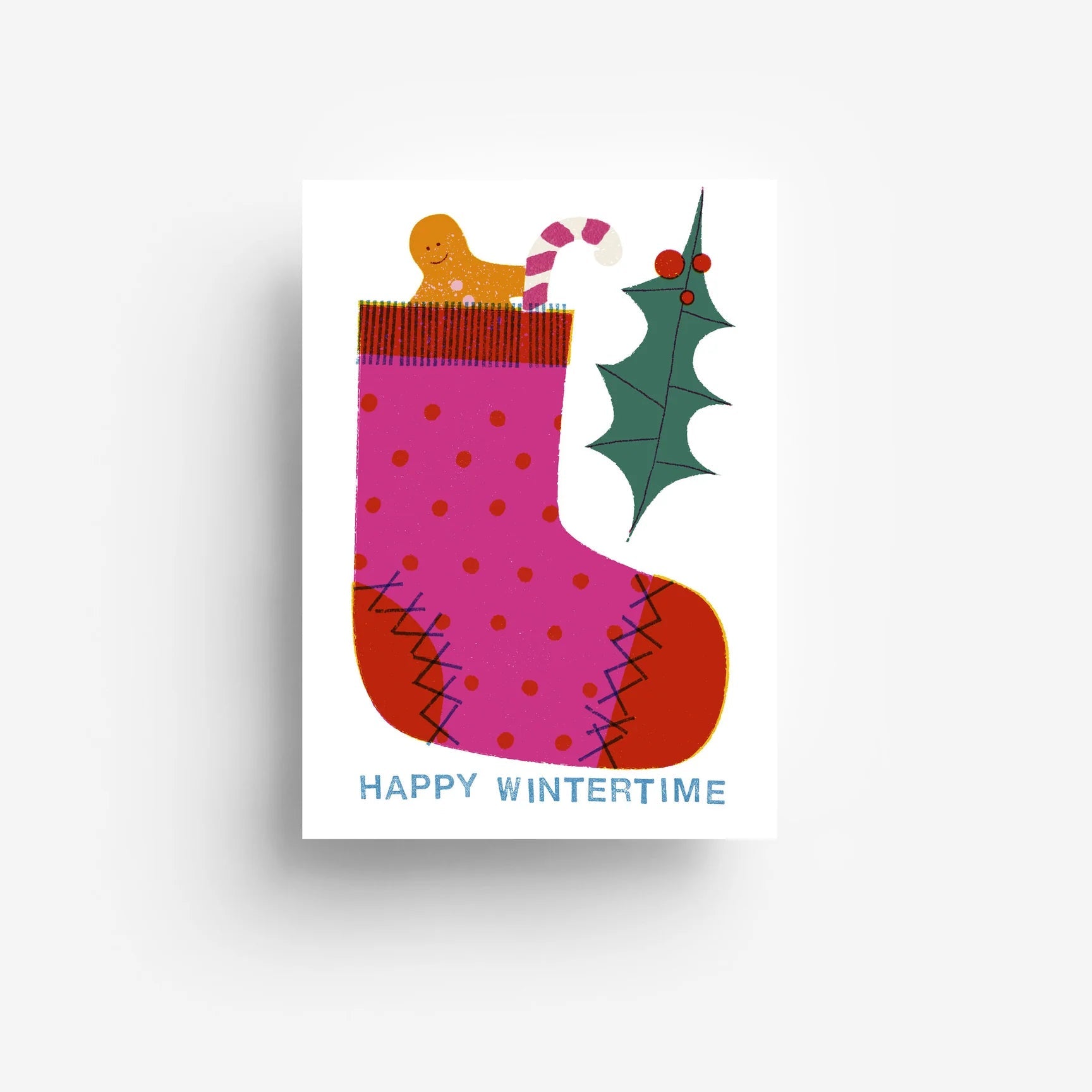 Eine festliche Karte mit einem rosa und rot gepunkteten Strumpf mit einem Lebkuchenkeks und einer Zuckerstange im Inneren, neben einem grünen Stechpalmenzweig mit roten Beeren. Der Text am unteren Rand lautet HAPPY WINTERTIME.