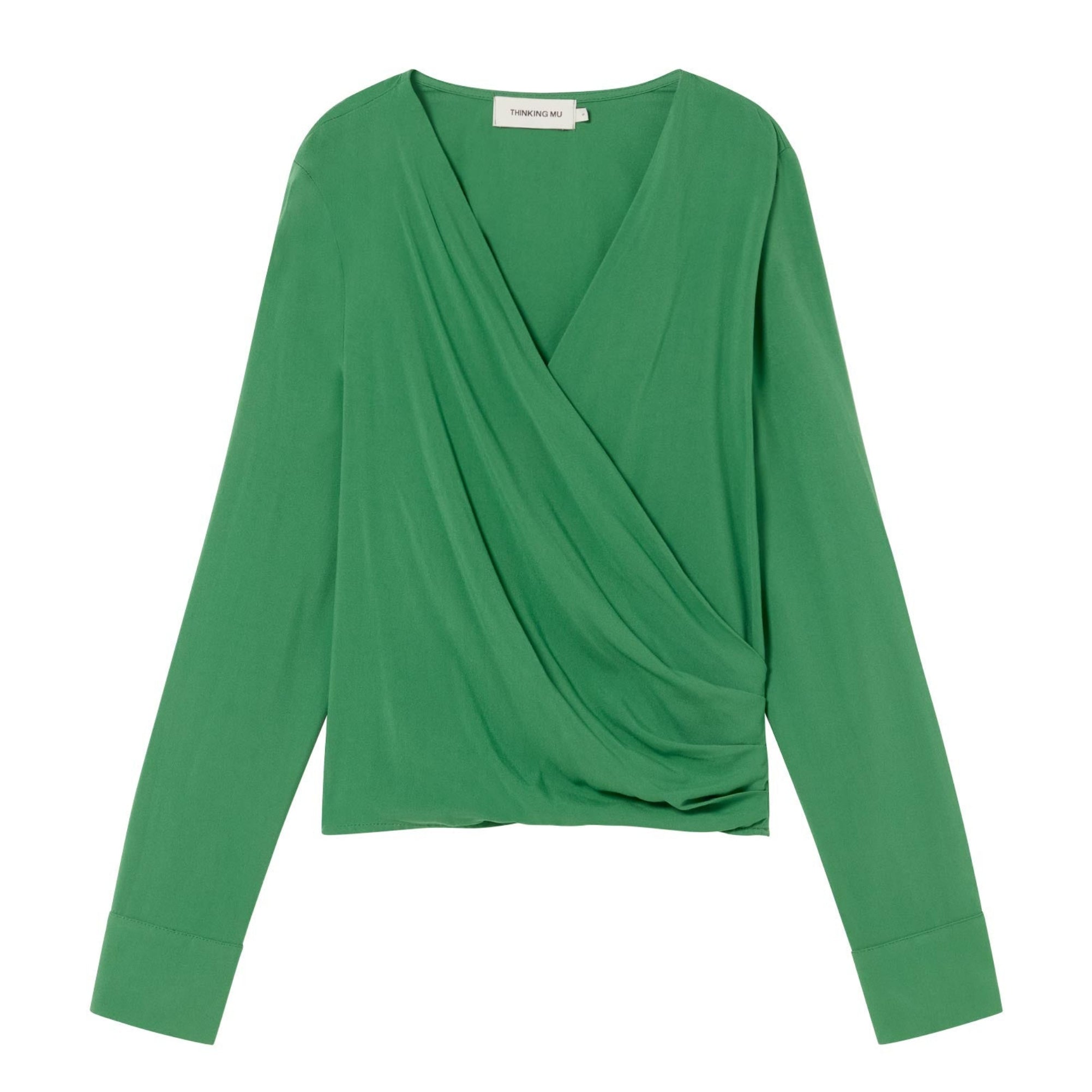 Eine langärmelige, grüne Bluse mit drapierter Wickeloptik und breiten Manschetten, flach auf weißem Grund.