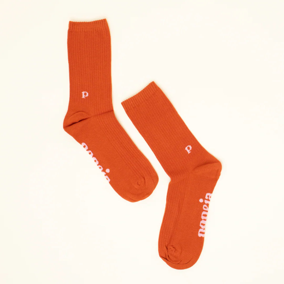 Ein Paar orangefarbene Socken mit einem kleinen weißen p in der Nähe des Knöchels und weißem Text entlang der Sohle auf einem schlichten, hellen Hintergrund.