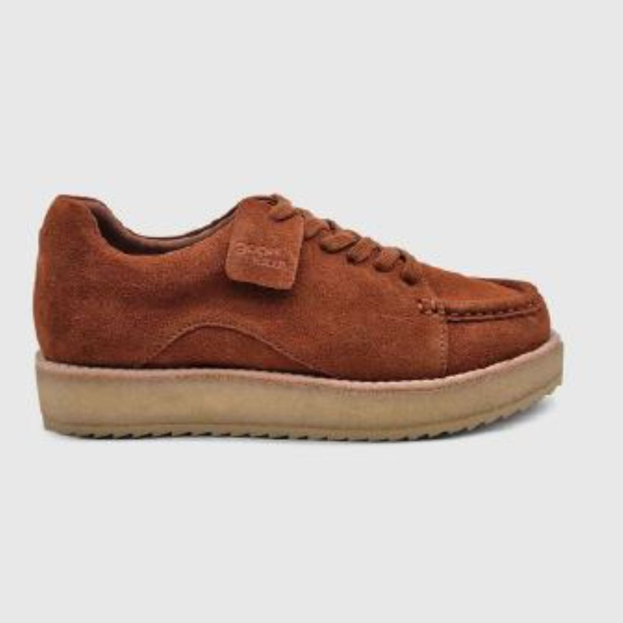 Ein brauner Wildleder-Schnürschuh mit einer dicken beigen Sohle, dargestellt in einer seitlichen Profilansicht vor einem schlichten hellgrauen Hintergrund.
