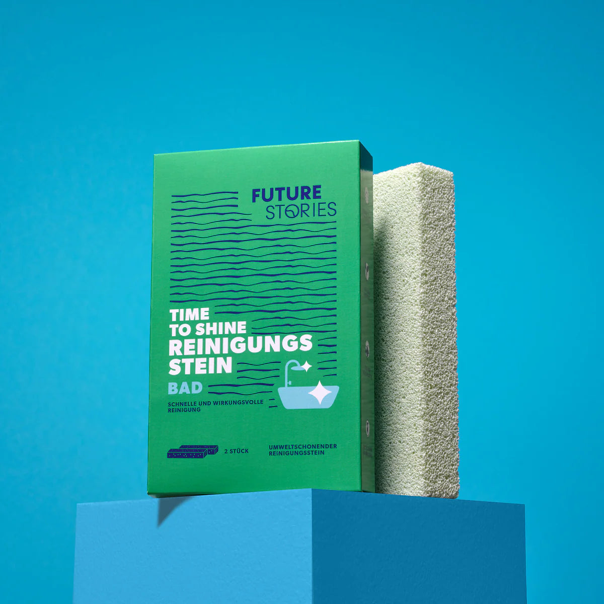 Eine grüne Box mit der Aufschrift Future Stories Time to Shine Reinigungsstein steht aufrecht neben einem beigen Reinigungsstein, beide auf einem blauen Sockel vor blauem Hintergrund.