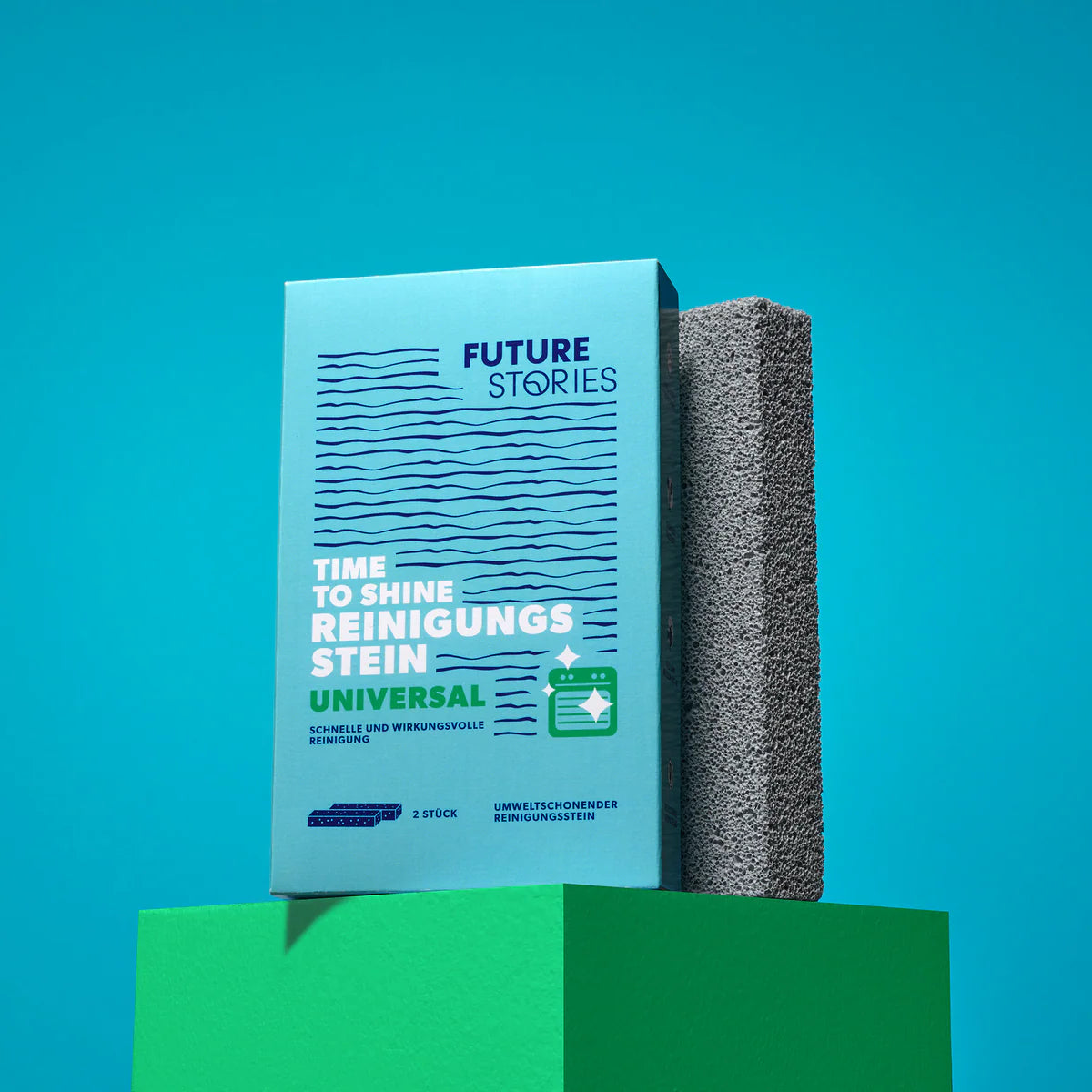 Eine blaue Schachtel mit der Aufschrift Future Stories Time to Shine Reinigungs Stein Universal steht aufrecht neben einem grauen Reinigungsstein auf einer grünen Plattform mit blauem Hintergrund.